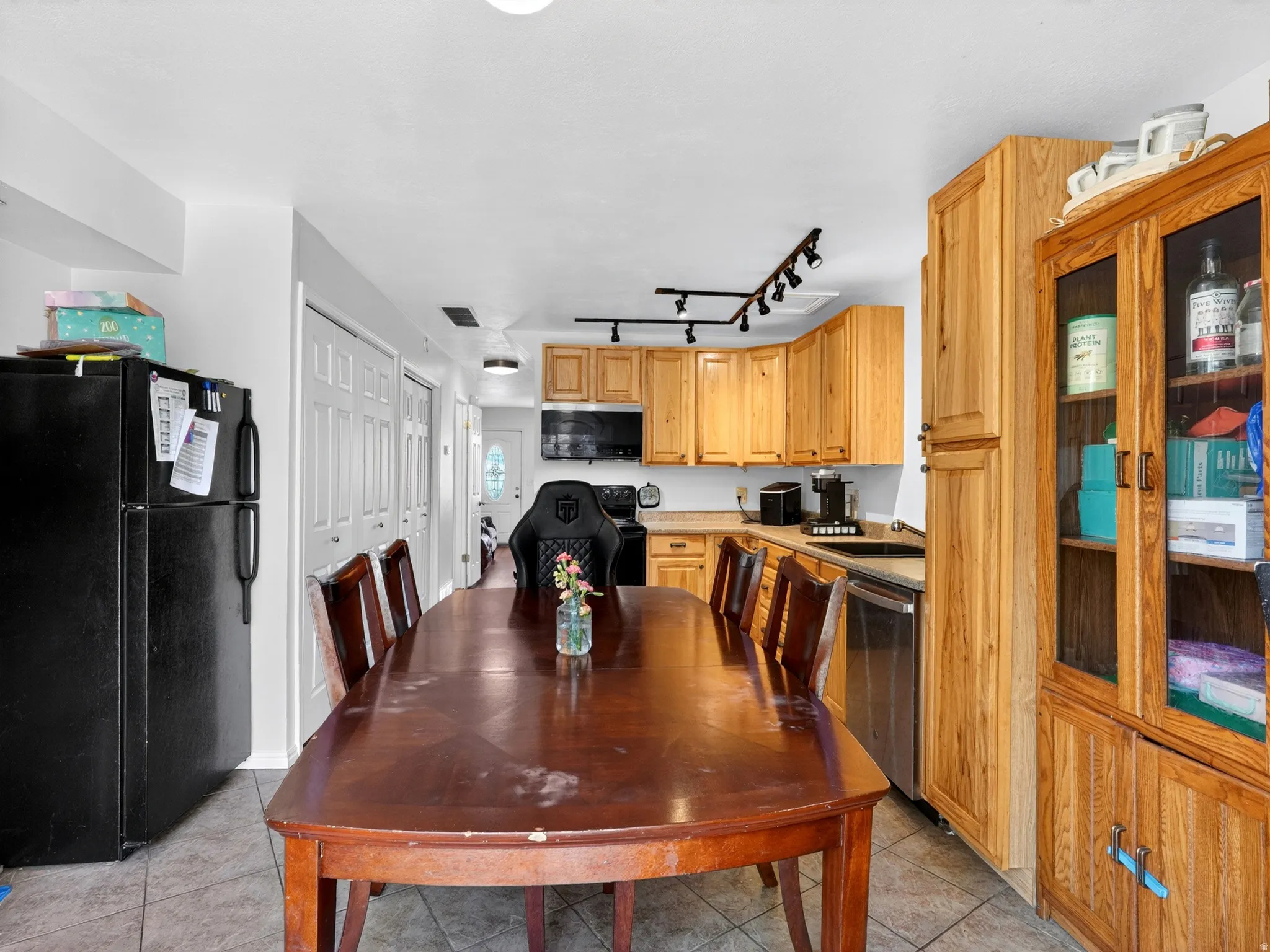 Kitchen and dining area featuring wood cabinetry, stainless steel dishwasher, track lighting, ceiling-mounted light fixture, and tile flooring