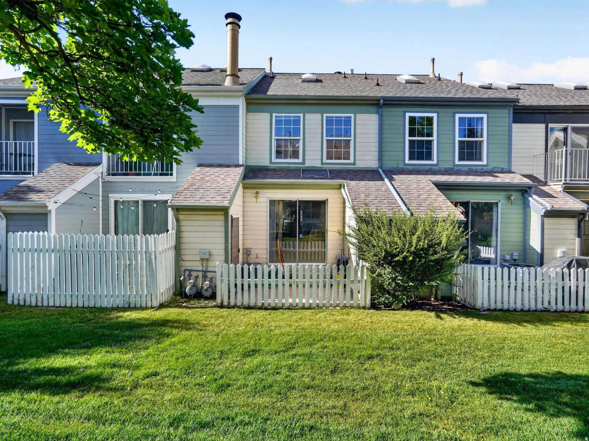 Rear exterior featuring a vibrant green lawn, white picket fencing, and multiple sliding glass doors