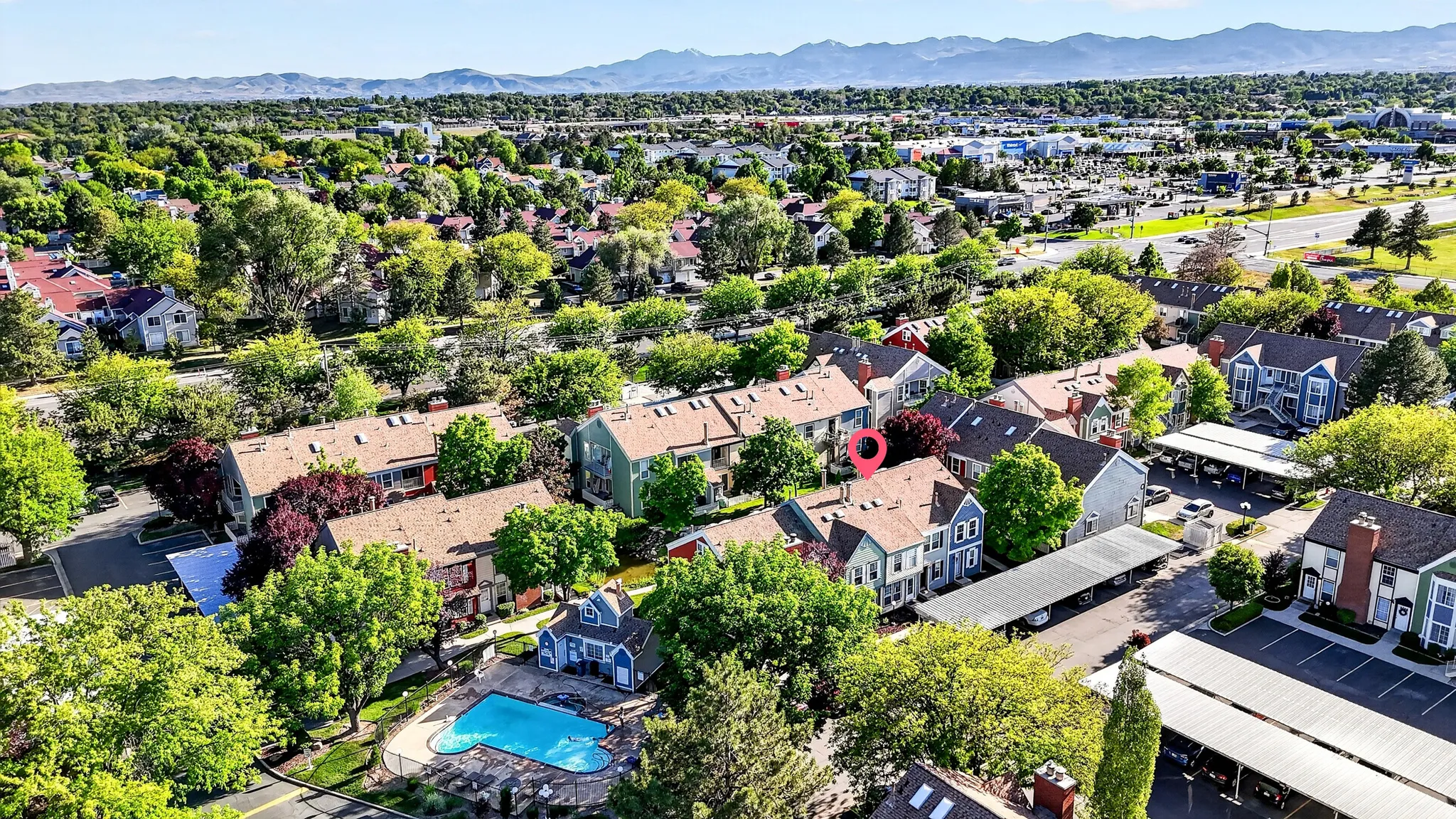 Aerial perspective highlighting a multi-unit complex with surrounding mature trees and distant mountain ranges