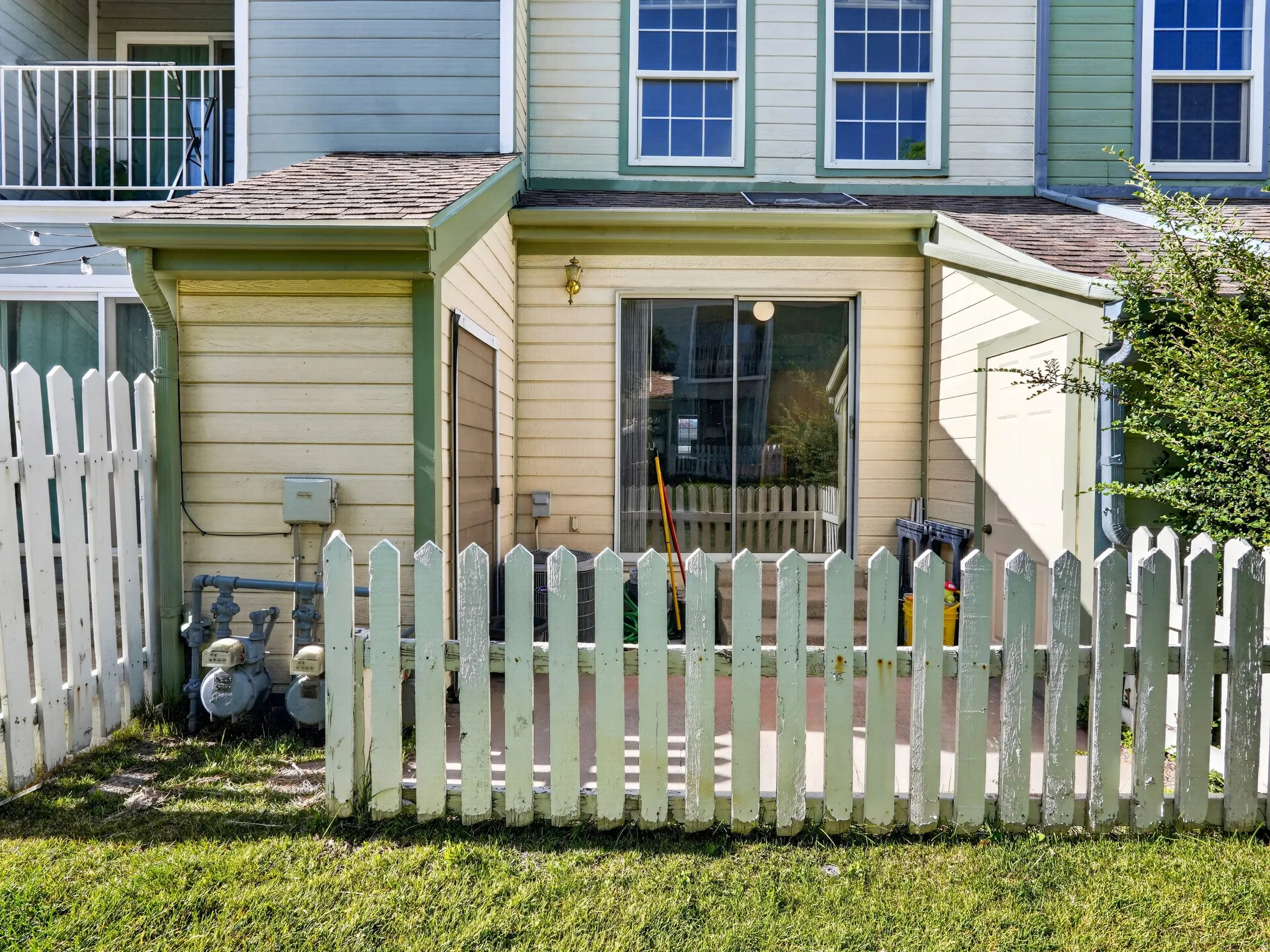 Private patio area bordered by a white picket fence, featuring a sliding glass door entry to the interior