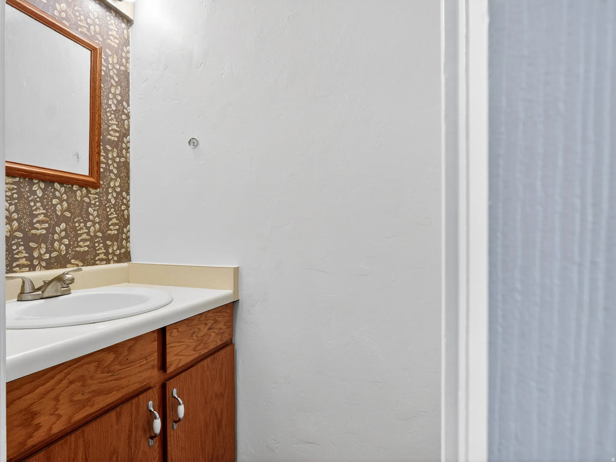 Bathroom vanity featuring a white oval sink, chrome faucet, and wood-finish cabinetry with white knob hardware