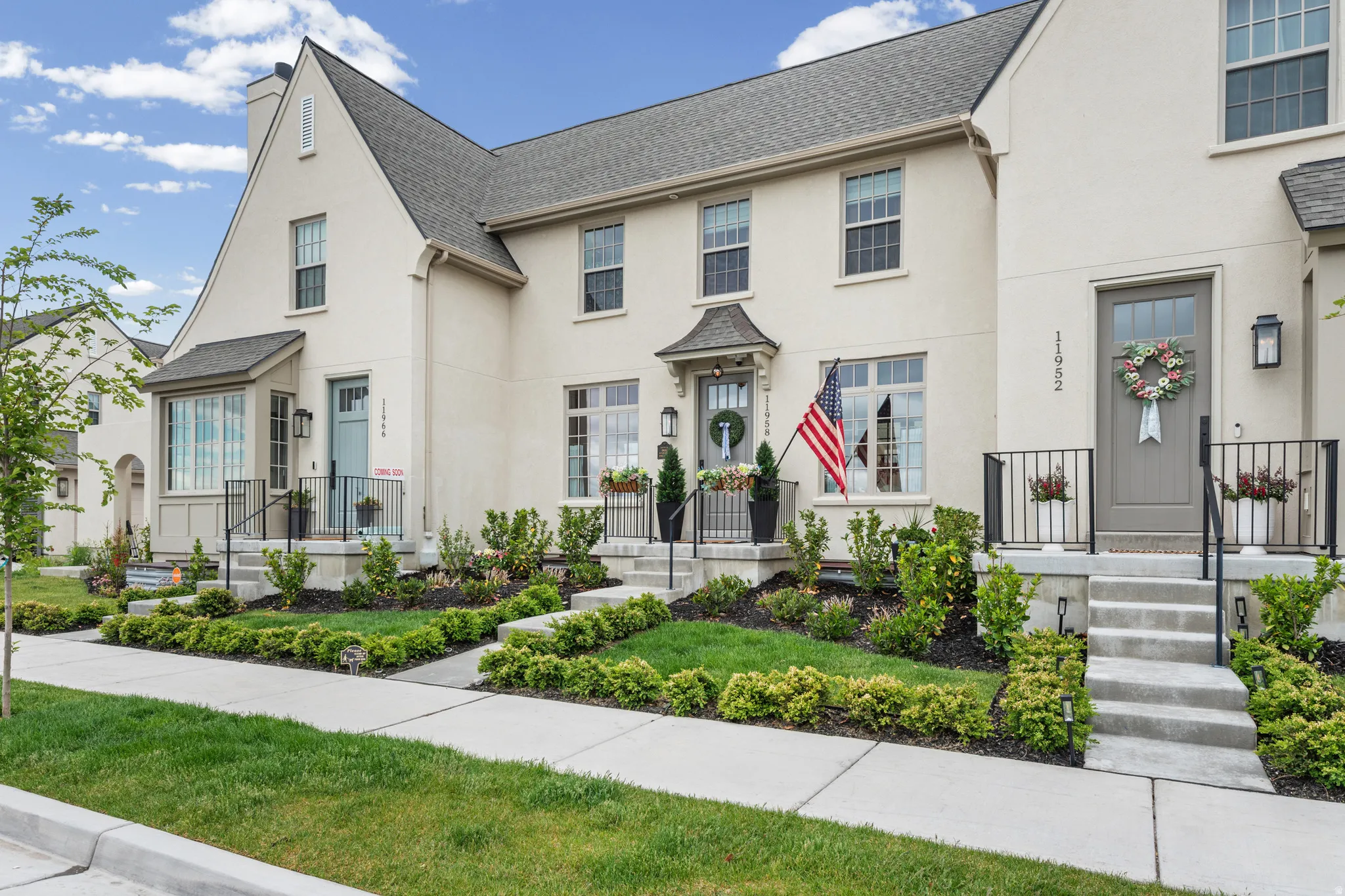 Stucco exterior featuring a gabled roofline, concrete entry stairs, black wrought iron railings, and manicured landscaping