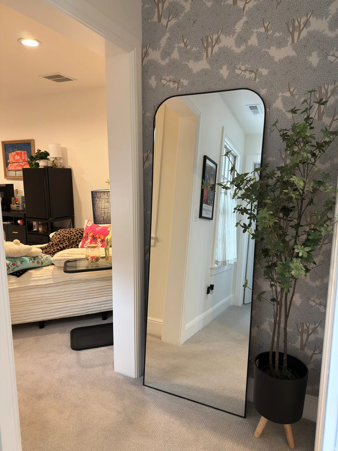 Textured wallpaper accentuates a full-length mirror, complemented by soft carpet flooring
