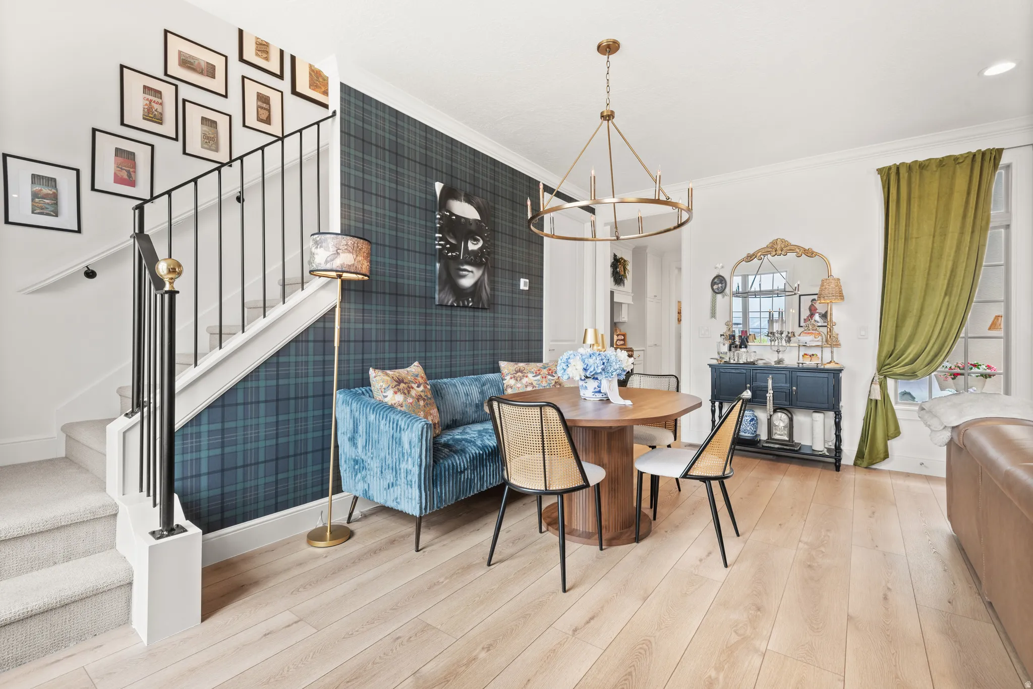 Inviting living area featuring light wood-finish flooring, a contemporary candelabra chandelier, a staircase with a black wrought iron railing with brass tops imported from Africa.