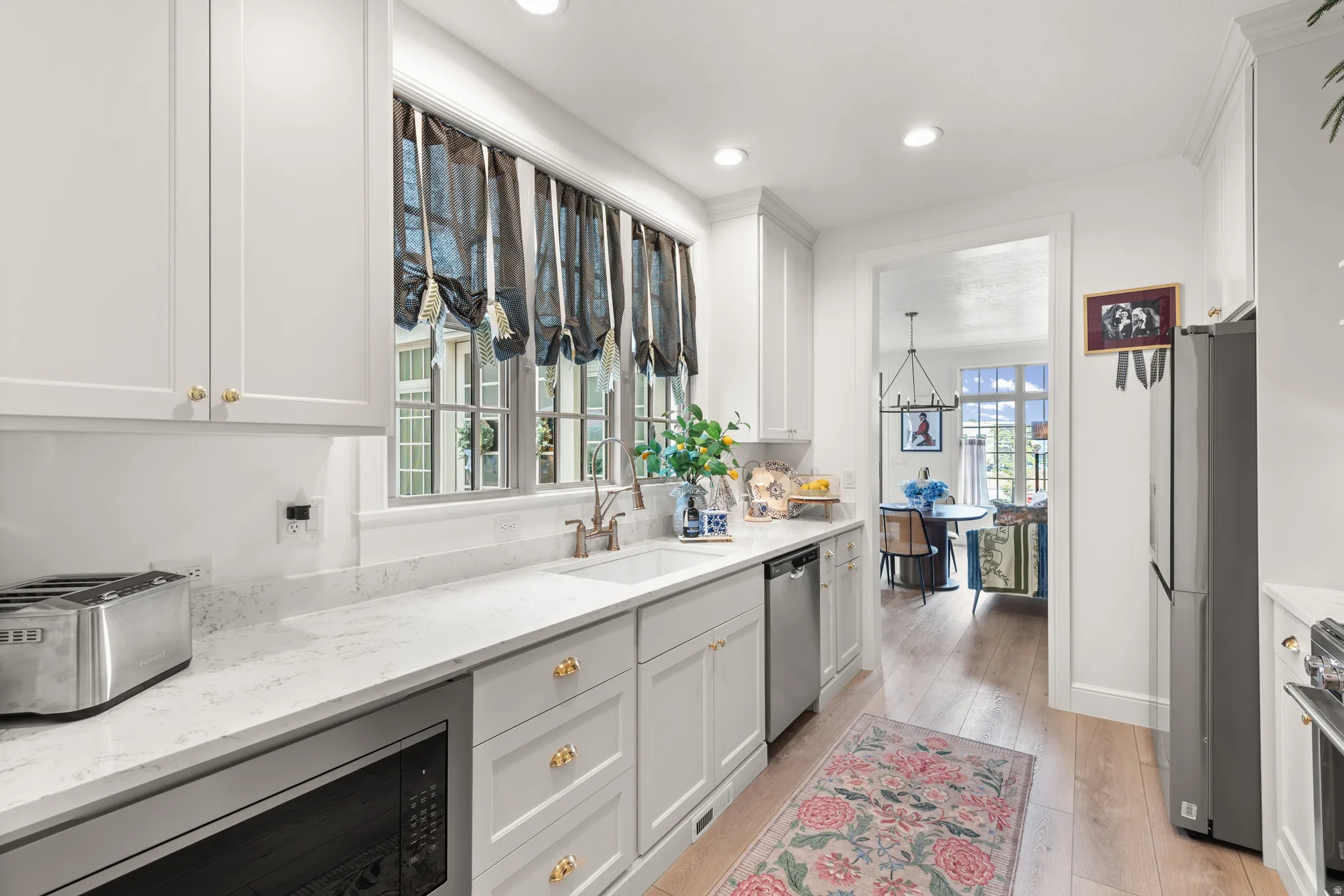White kitchen featuring recessed lighting, light-toned wood-finish flooring, and white cabinetry with gold-tone hardware imported from the UK.