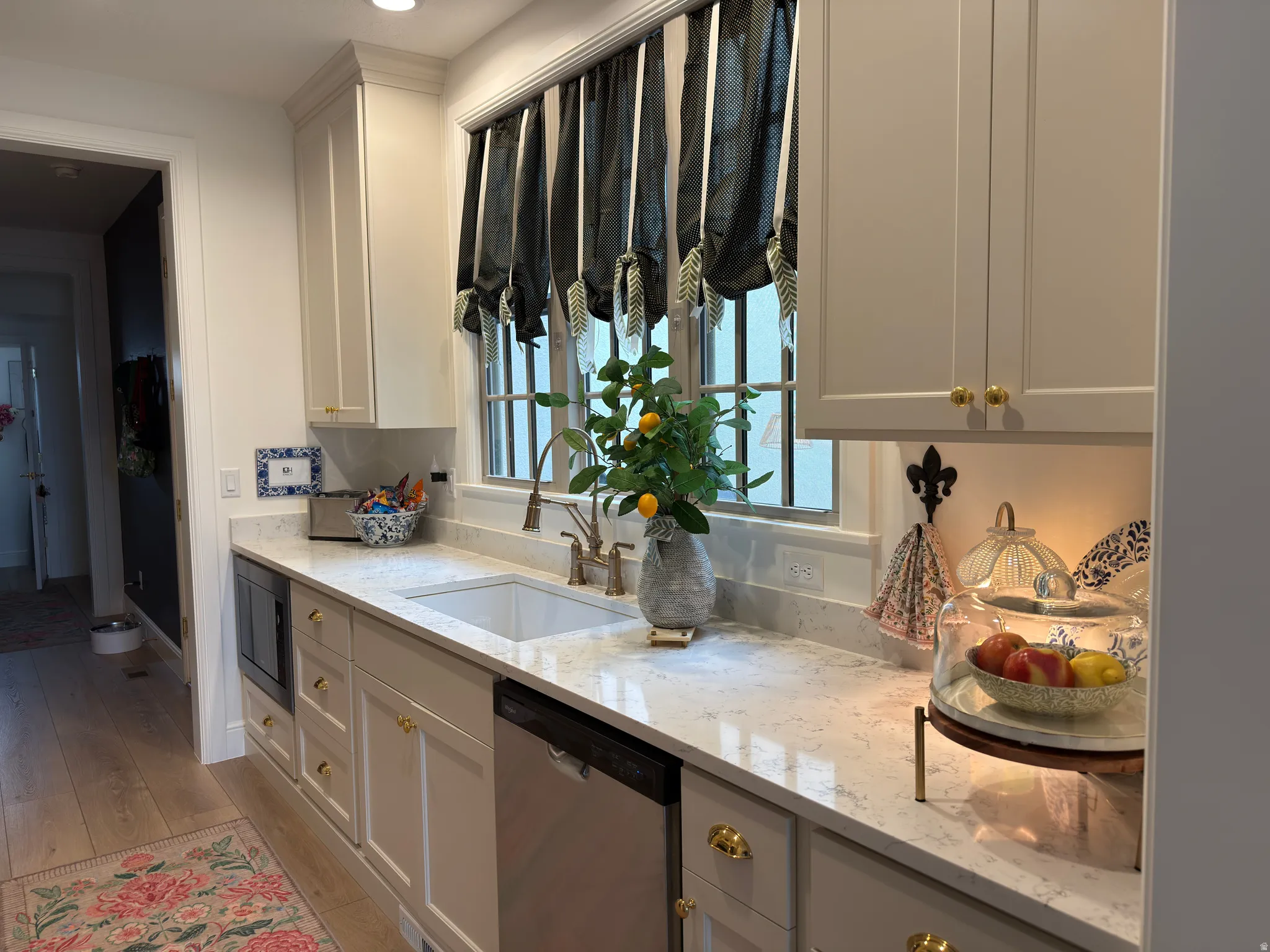 Kitchen featuring light-toned cabinetry with gold-toned hardware, a stainless steel dishwasher, and an under-counter microwave