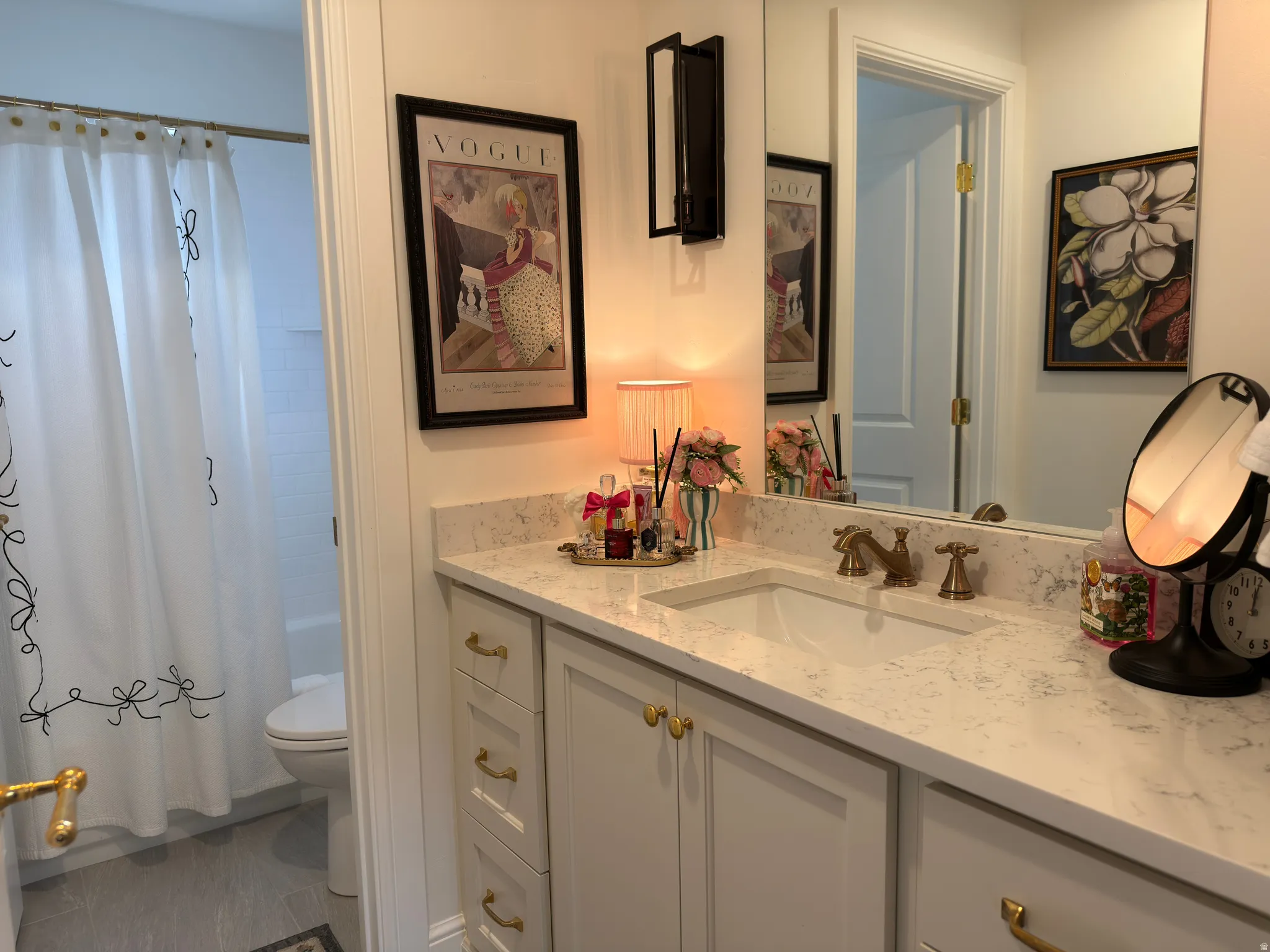 Bathroom featuring a white vanity with gold-tone hardware, a light-colored countertop with integrated sink, and brass-finish faucet