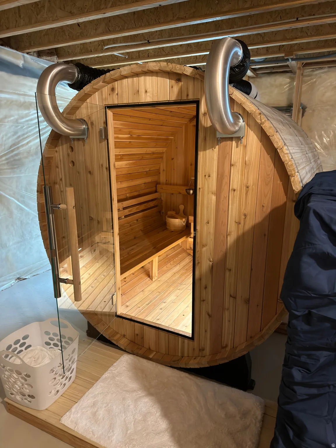 Barrel sauna with a clear glass door, interior wood benches, and exterior metal ventilation pipes