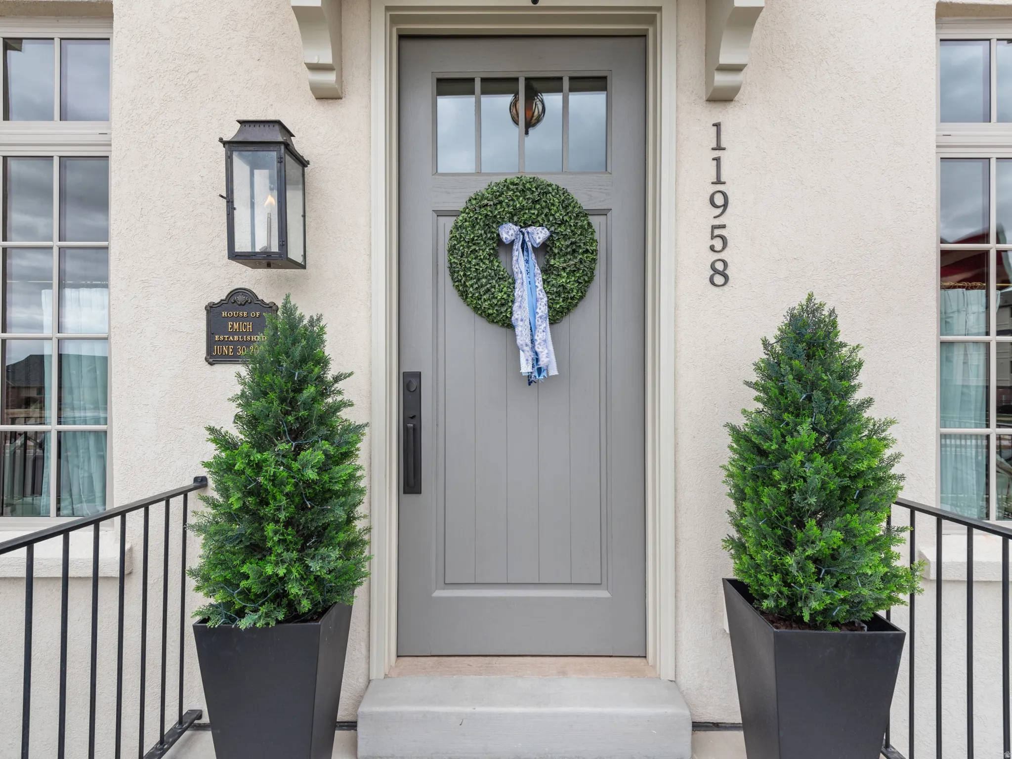 Entryway featuring a grey paneled door with window inserts, stucco exterior, and black wrought iron railings