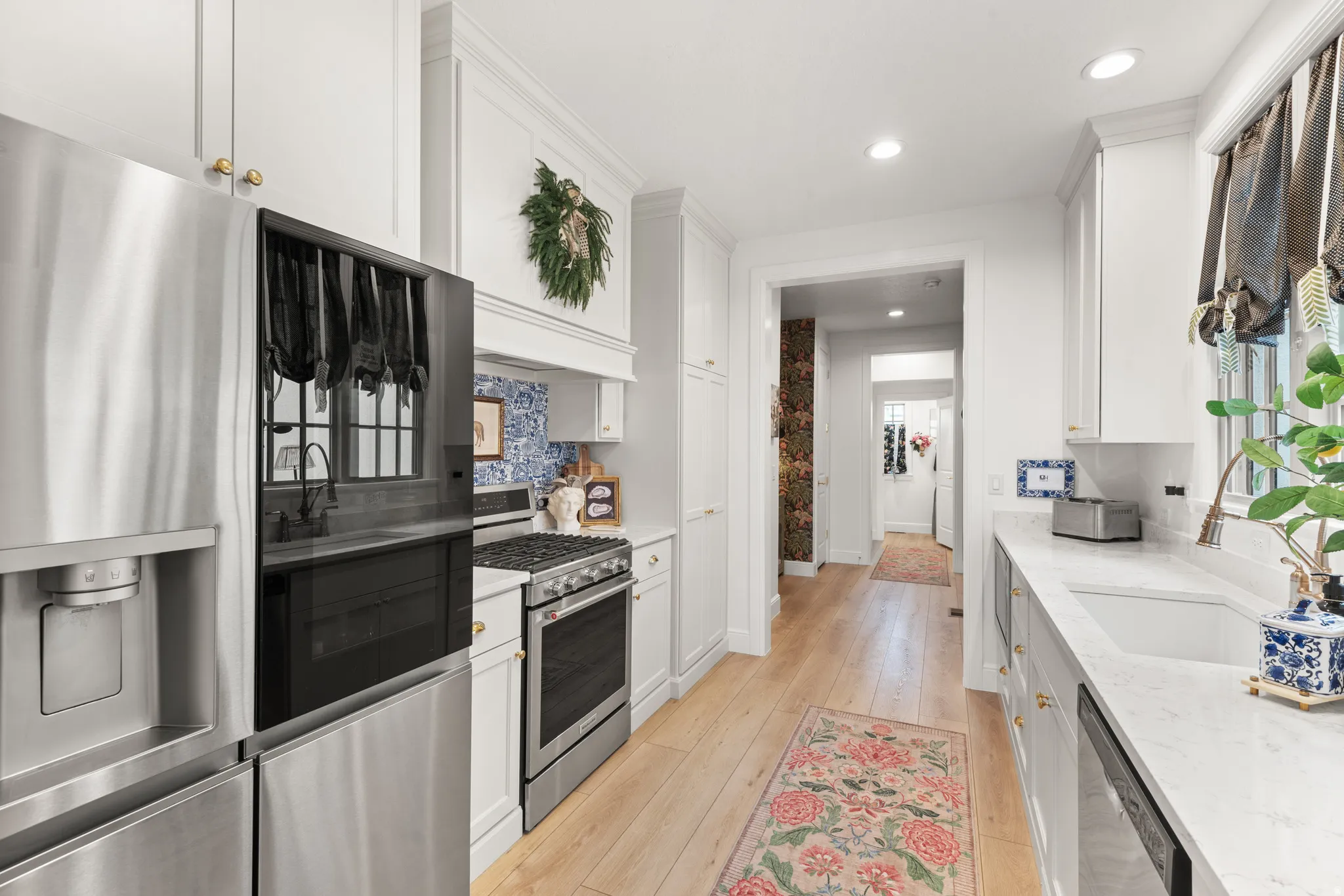 Galley kitchen featuring stainless steel appliances, light wood-finish flooring, white cabinetry with gold-toned hardware imported from the UK, white quartz countertops, and recessed lighting