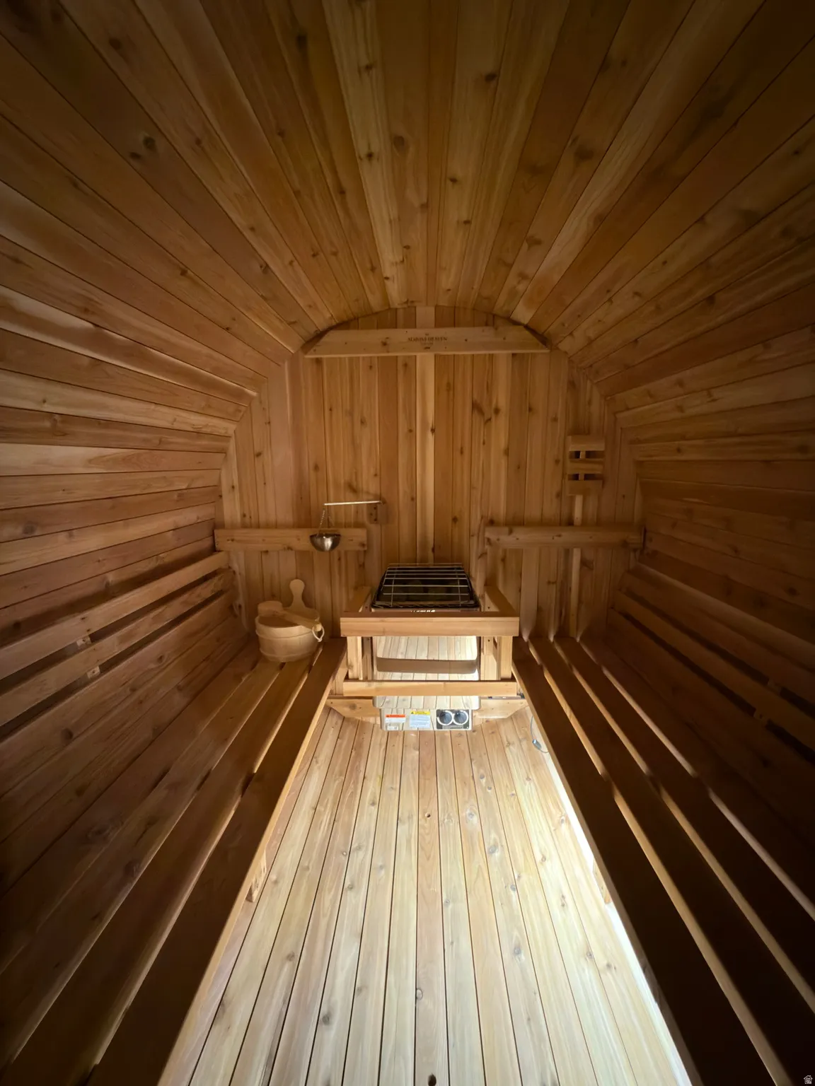Interior wood-paneled barrel sauna featuring built-in benches, a heating unit, and integrated ventilation