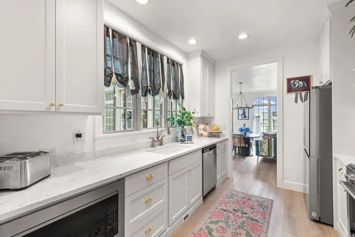 White kitchen featuring recessed lighting, light-toned wood-finish flooring, and white cabinetry with gold-tone hardware imported from the UK.