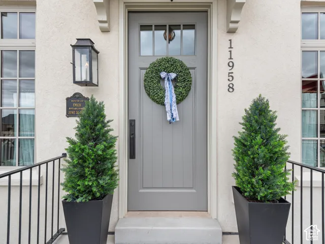 Entryway featuring a grey paneled door with window inserts, stucco exterior, and black wrought iron railings