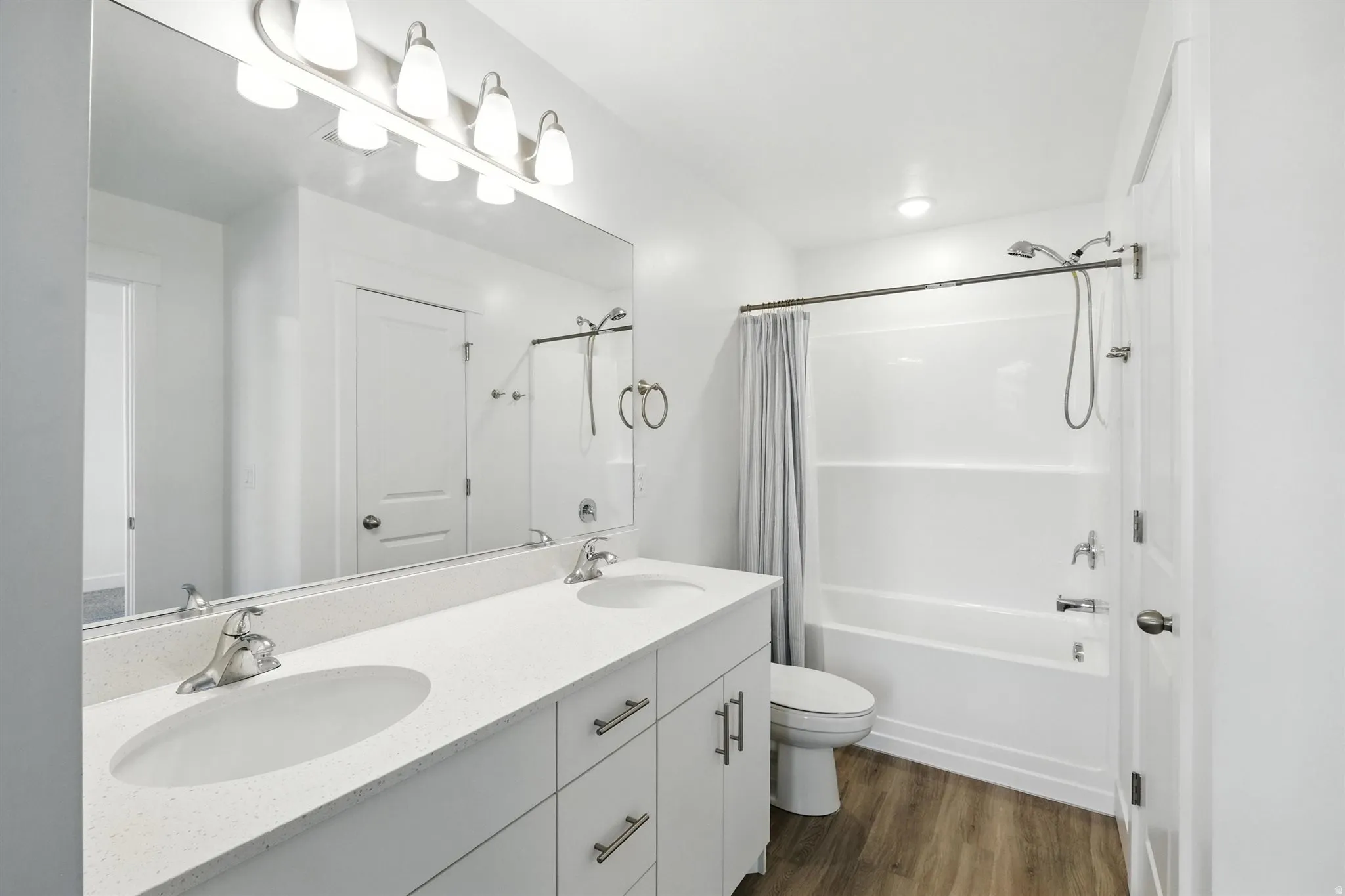 Modern bathroom featuring a dual-sink vanity with a light-toned countertop, brushed nickel hardware, and wood-finish flooring
