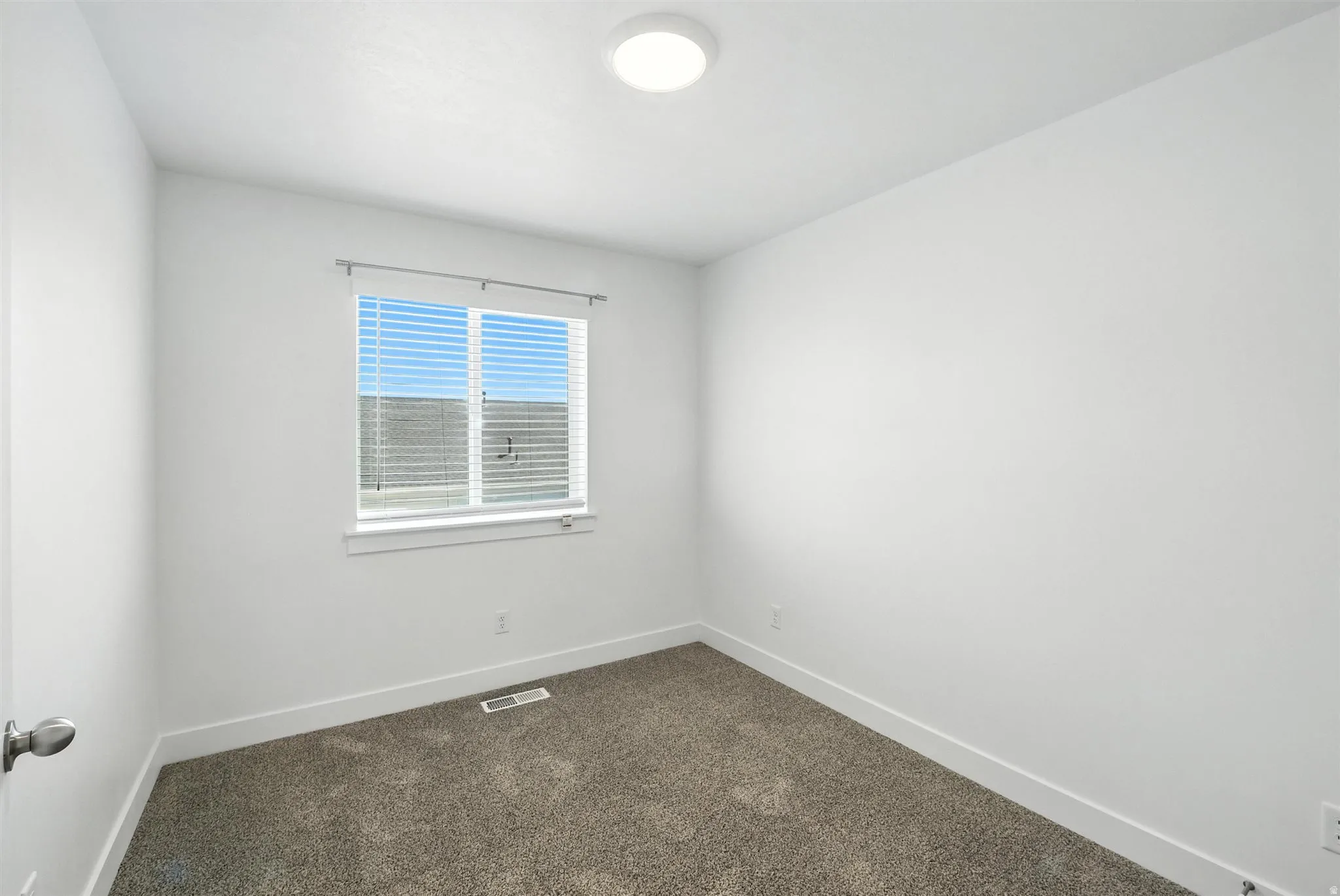 Bright room featuring a window with horizontal blinds, neutral-toned carpet flooring, white walls, white baseboards, and a flush-mount ceiling light