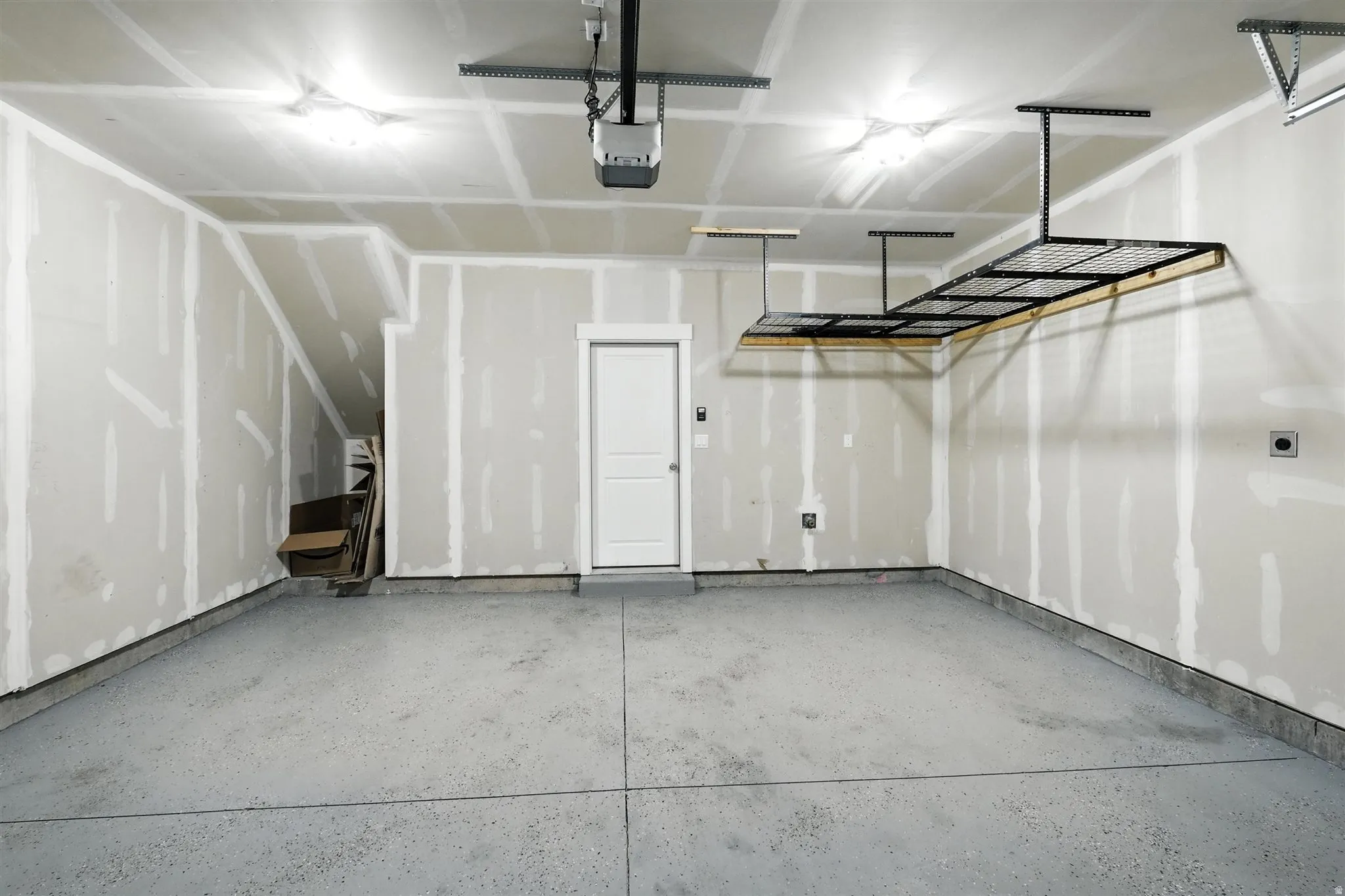 Spacious garage featuring a durable epoxy floor coating, overhead storage rack system, and a convenient interior access door