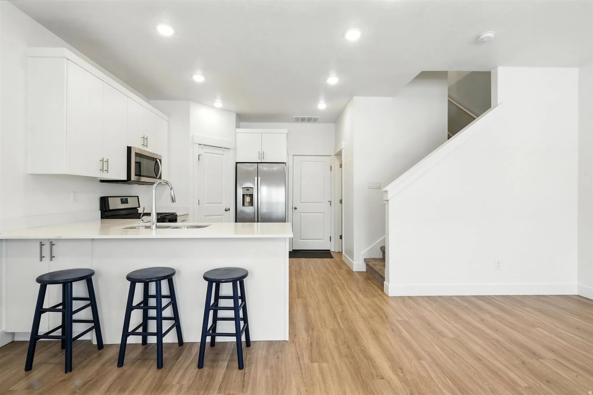Open-concept kitchen featuring white cabinetry, stainless steel appliances, a breakfast bar, and recessed lighting