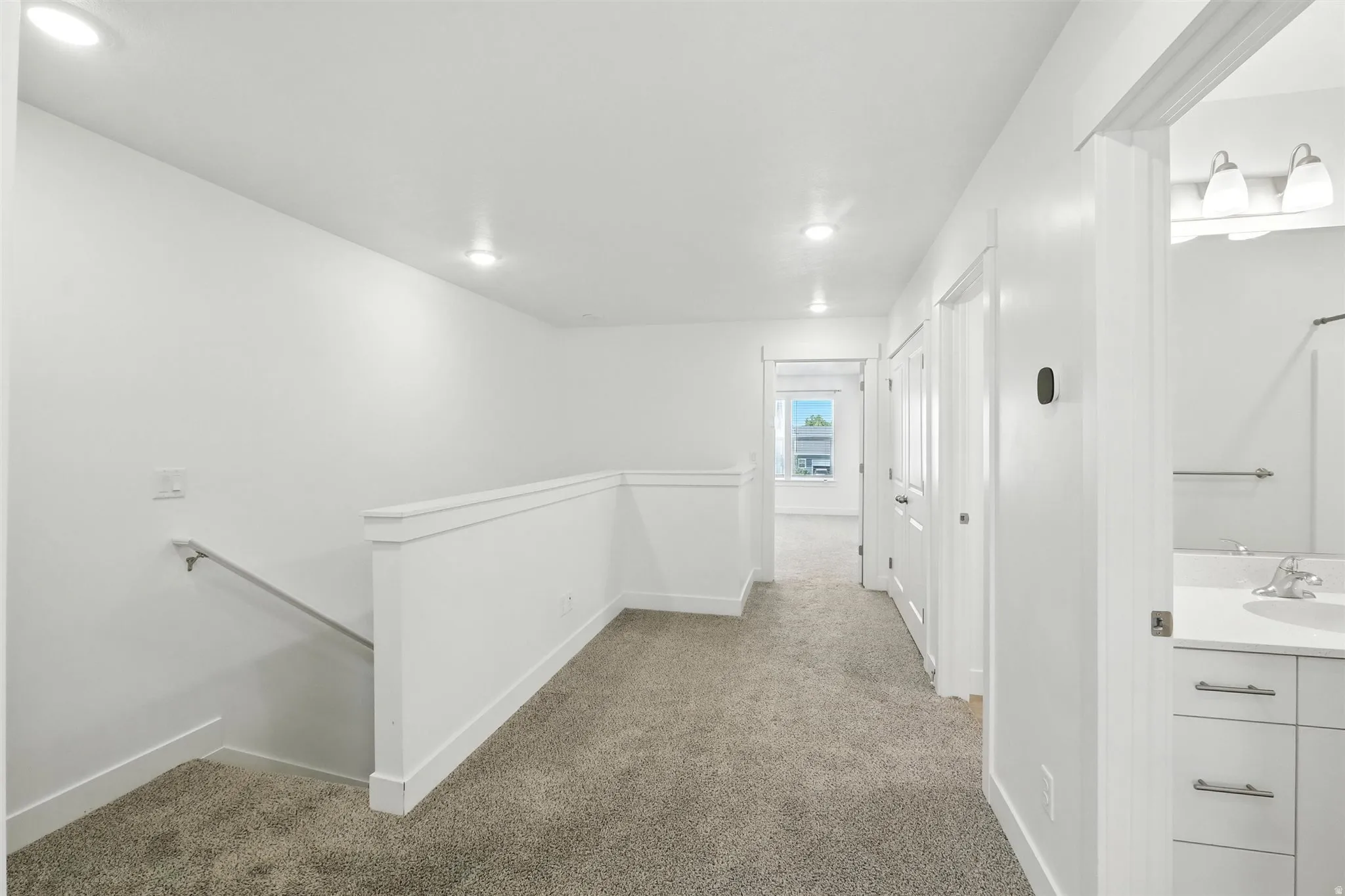 Upper-level hallway featuring neutral carpeting, recessed lighting, white walls, and a white railing