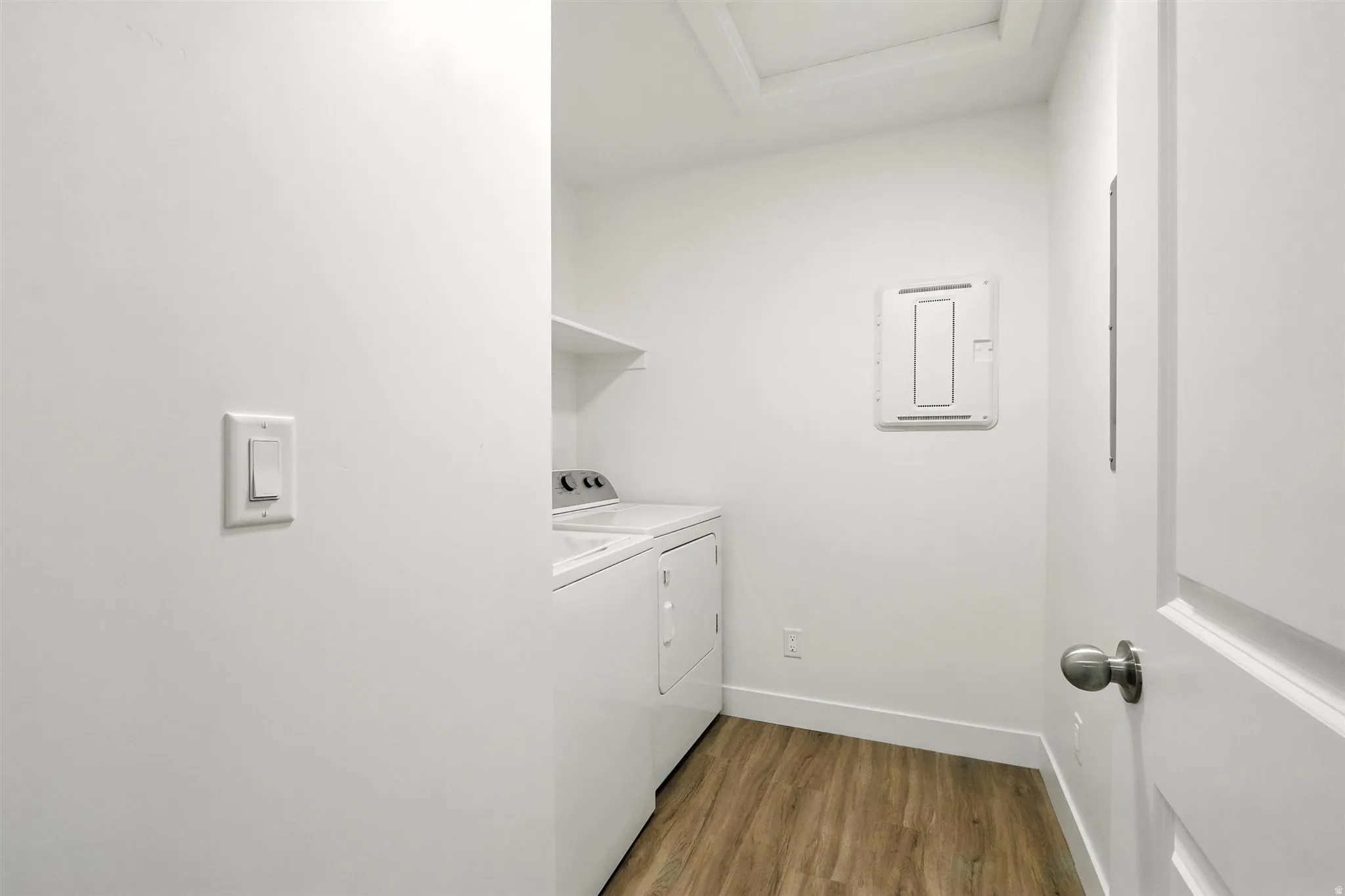 Dedicated laundry space featuring wood-finish flooring, white walls, and a built-in overhead shelf