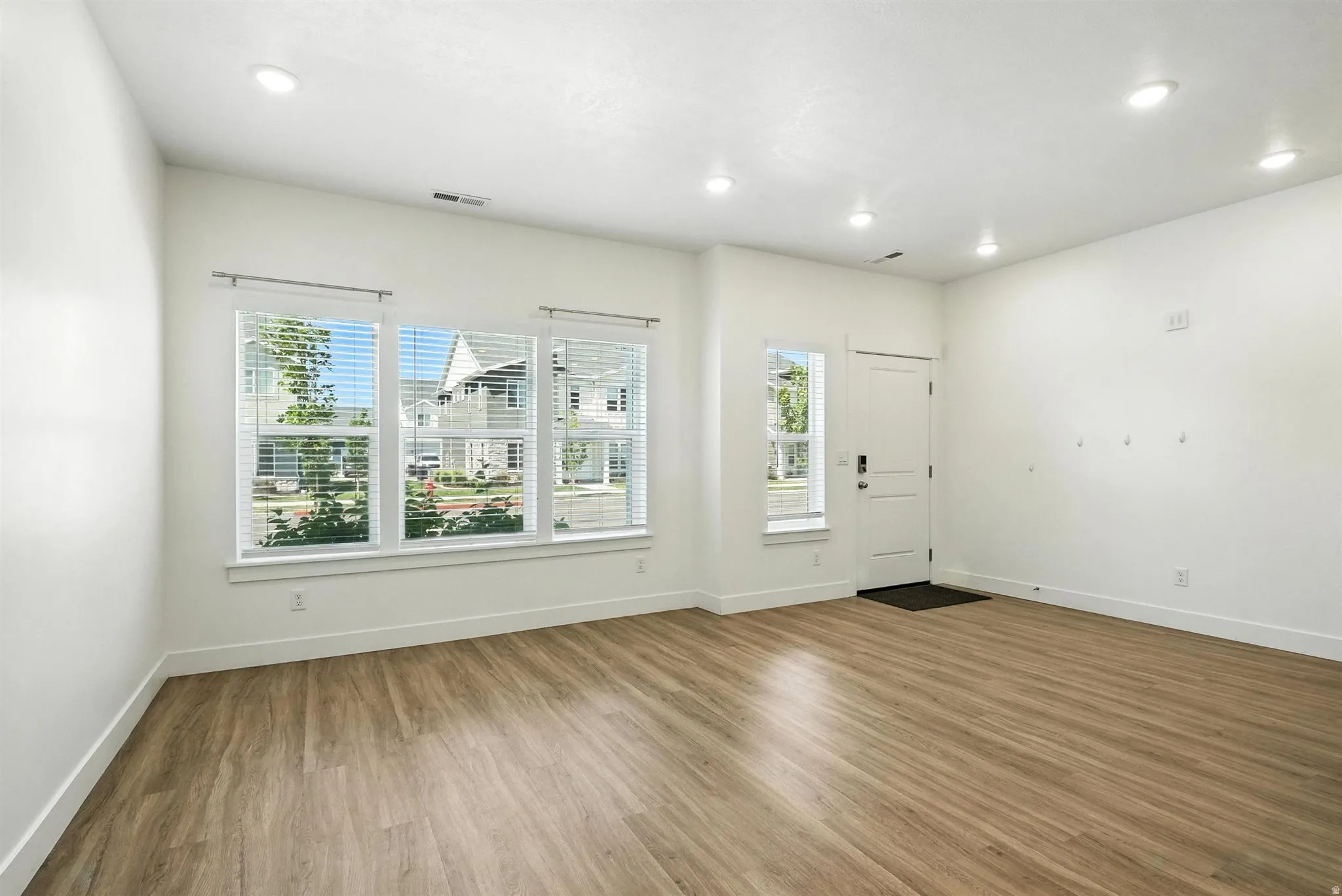 Spacious room featuring wood-finish flooring, recessed lighting, and multiple windows with blinds