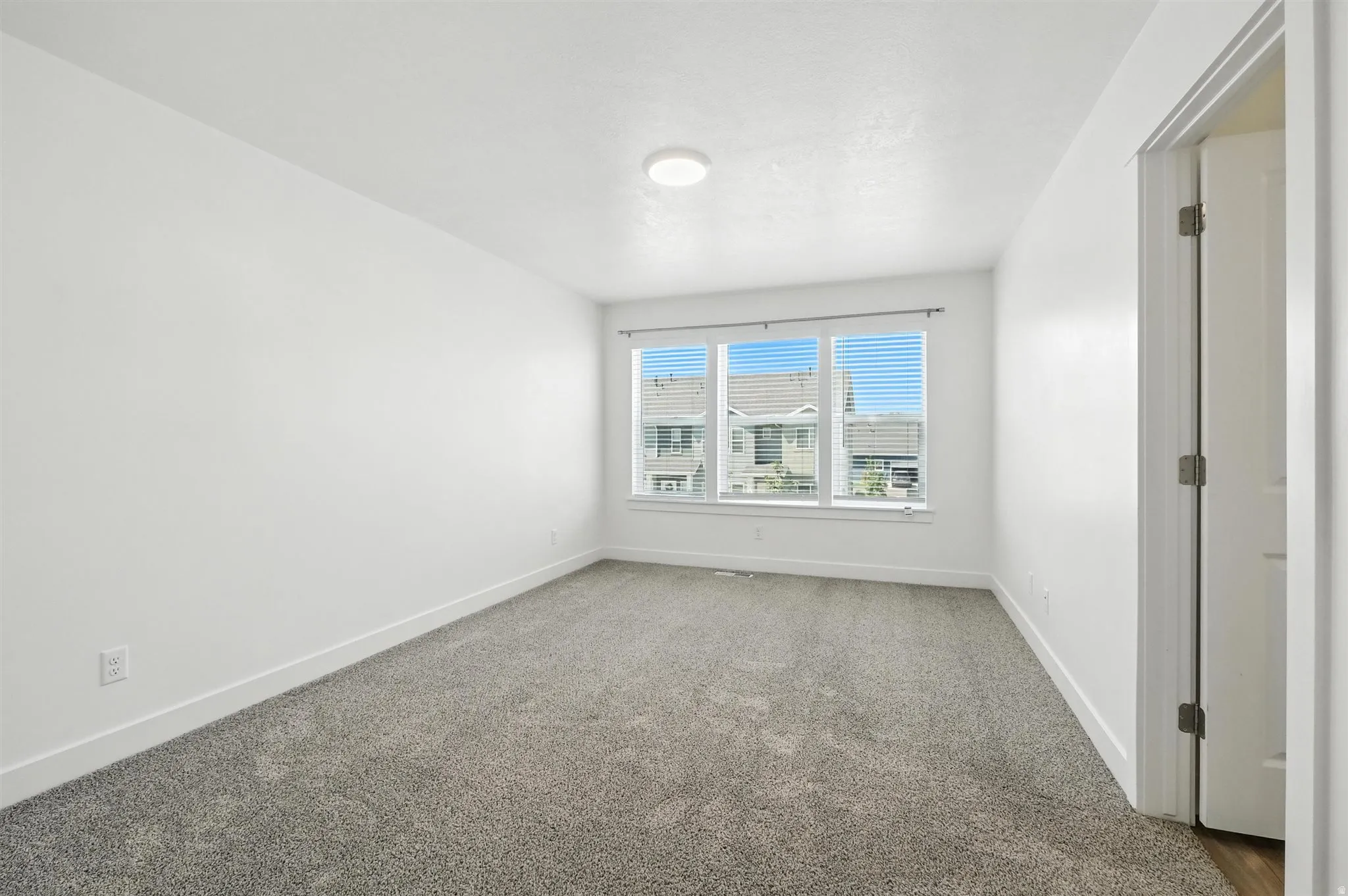 Room featuring light-toned carpeting, white walls, and a multi-pane window with blinds