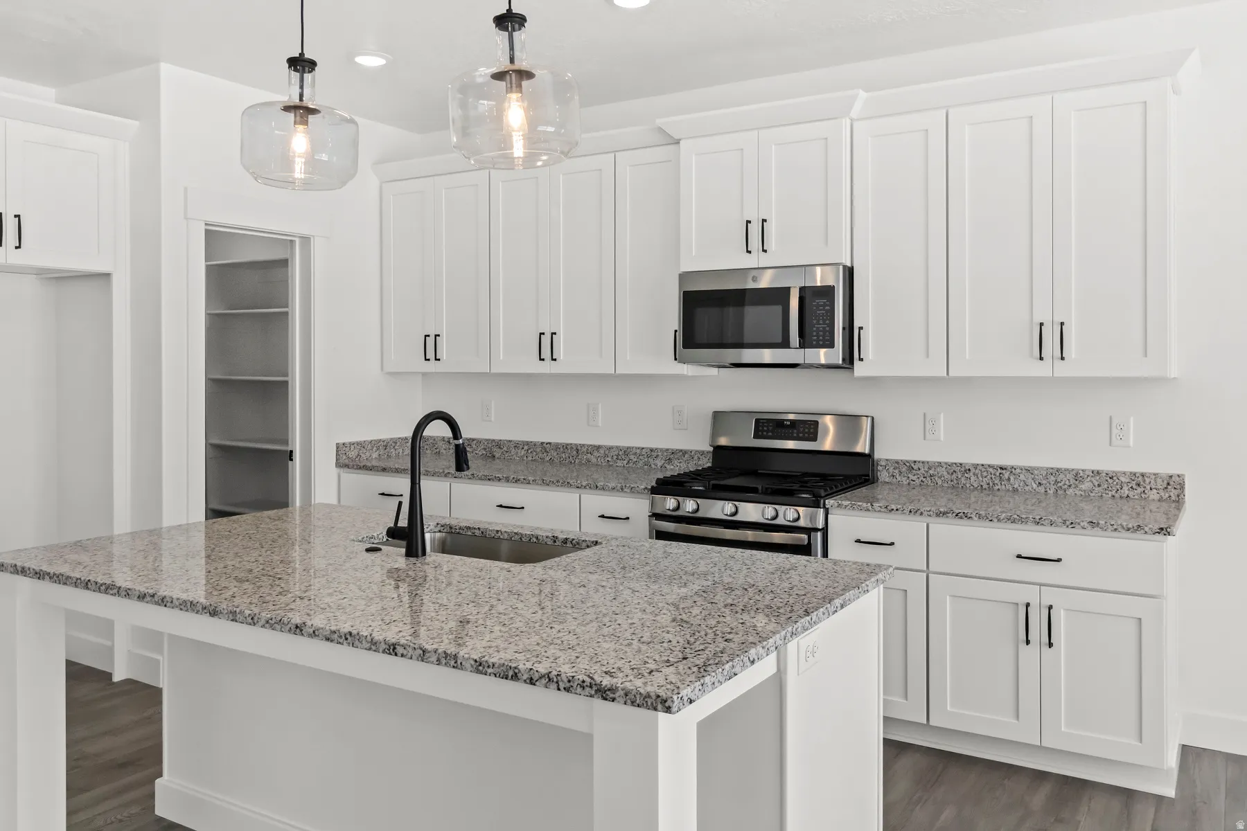 Kitchen featuring an oversized island with an undermount sink and matte black faucet, white shaker cabinetry, stainless steel appliances