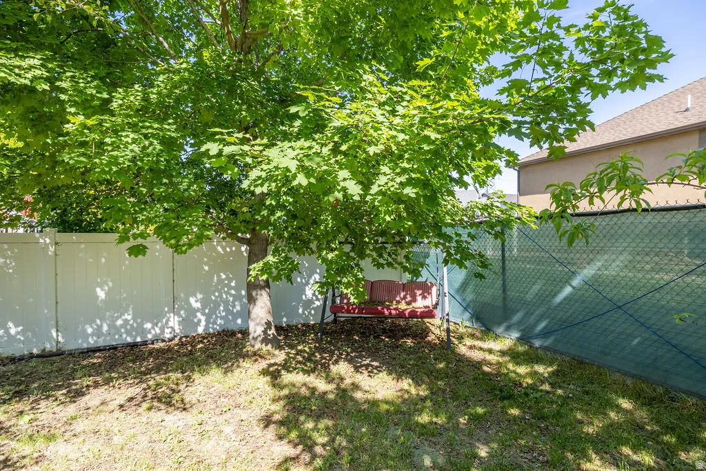 Expansive backyard featuring a mature shade tree, a white privacy fence, and a chain-link fence with privacy screening