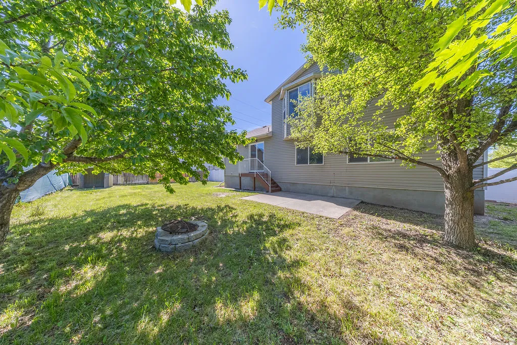 Backyard featuring mature trees, a concrete patio, and a built-in stone fire pit