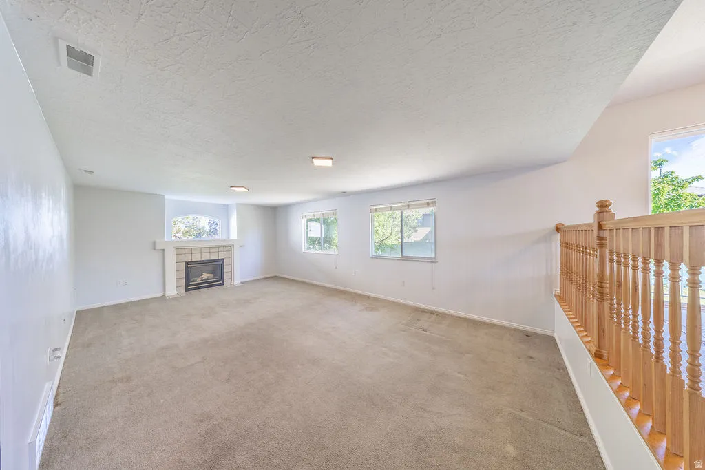 Spacious room featuring a fireplace with a tile surround and mantel, multiple windows providing natural light, recessed lighting, and a wood baluster railing