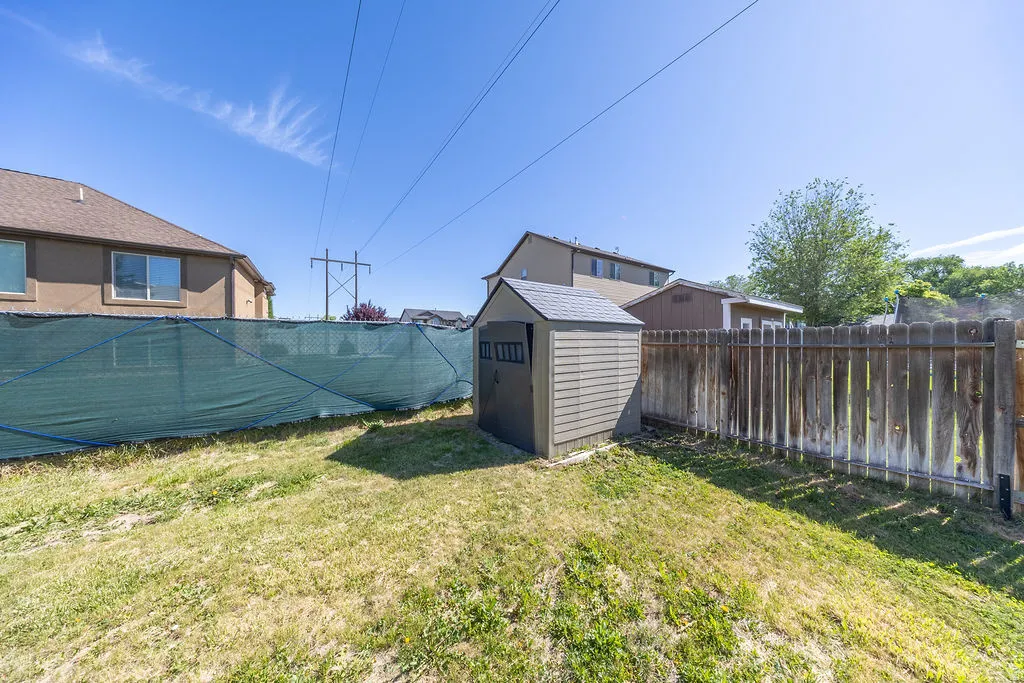Backyard featuring a storage shed with a shingle roof and slat siding, a wood fence, and a green privacy screen