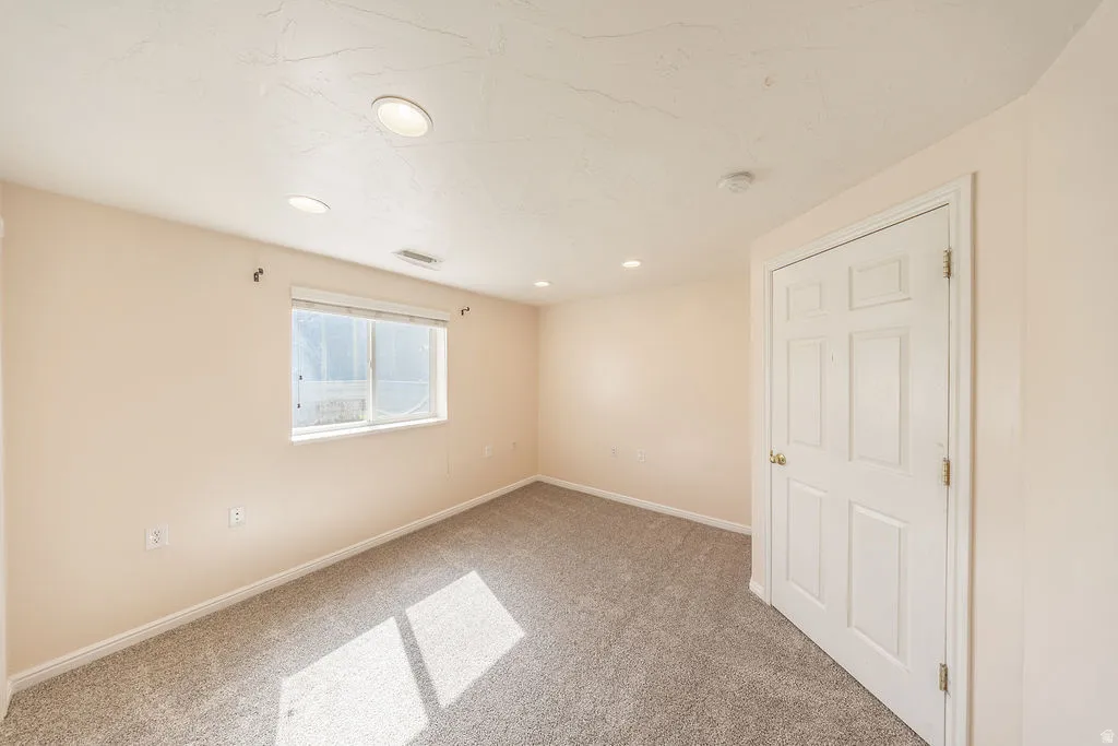 Carpeted basement room with closet, recessed lighting, and a window with blinds