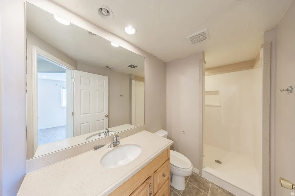 Basement bathroom featuring a vanity with an integrated sink, a large wall-mounted mirror, and a walk-in shower with a built-in niche