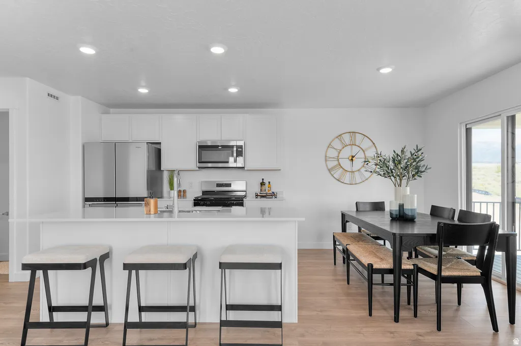 Open-concept kitchen and dining area featuring white cabinetry, stainless steel appliances, a kitchen island with seating, and wood-finish flooring