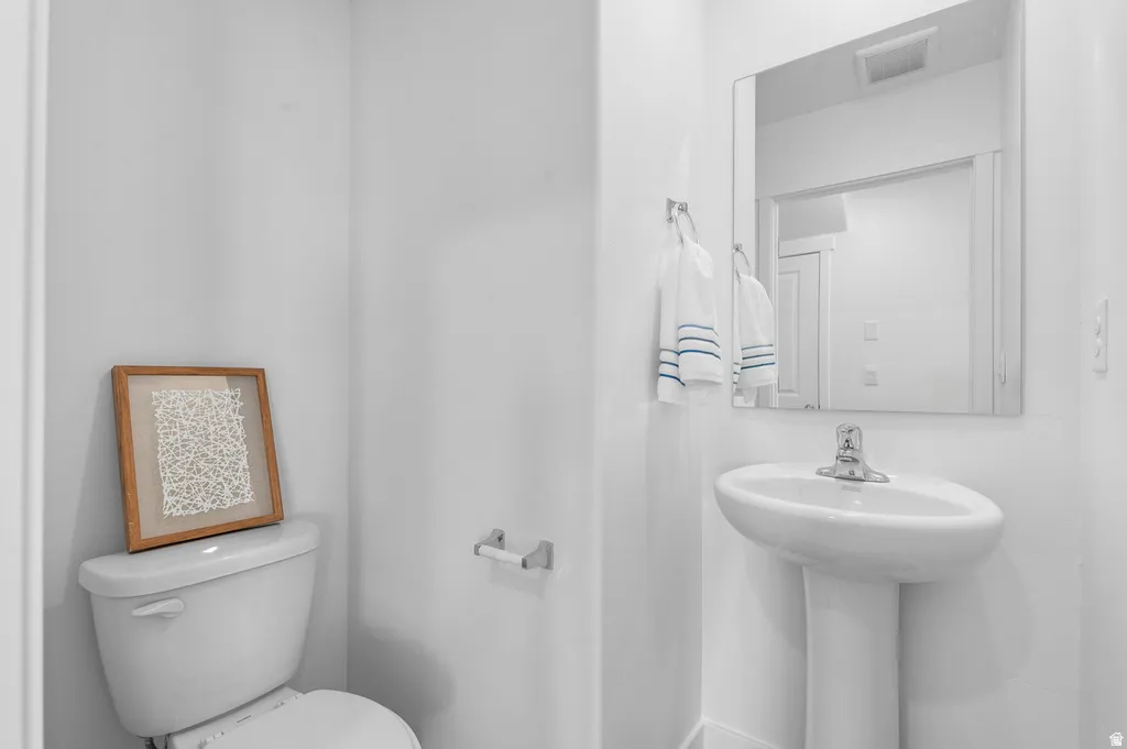 Pedestal sink with chrome faucet, a rectangular wall-mounted mirror, and a toilet with a white tank