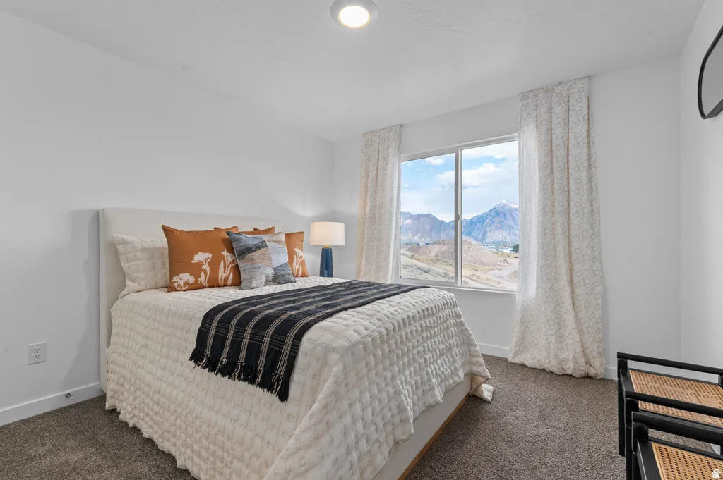 Bright bedroom featuring a large window with mountain scenery, plush carpet flooring, white walls, and a ceiling-mounted light fixture