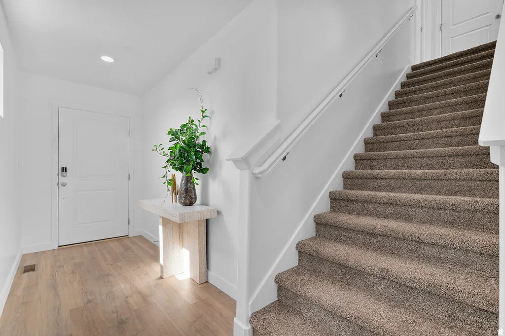 Entryway featuring wood-finish flooring, a white paneled door with contemporary hardware, and a carpeted staircase with a white handrail