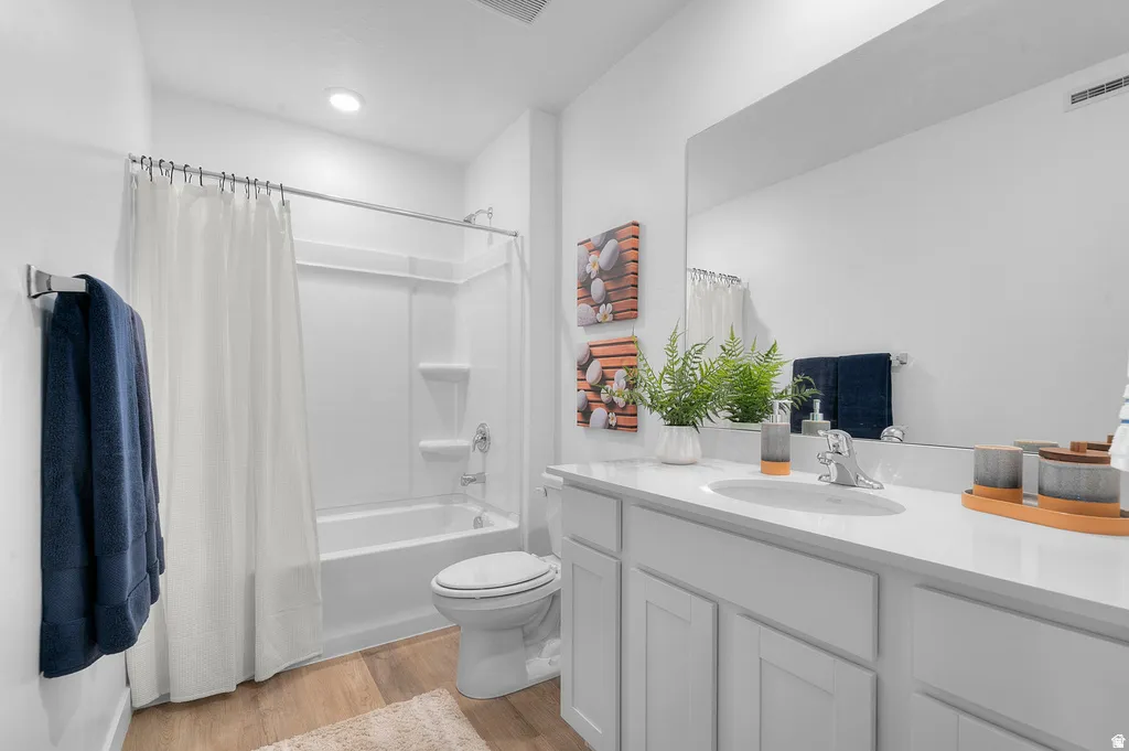 Bathroom featuring a white vanity with an integrated sink, a large wall-mounted mirror, white paneled cabinetry, and wood-finish flooring