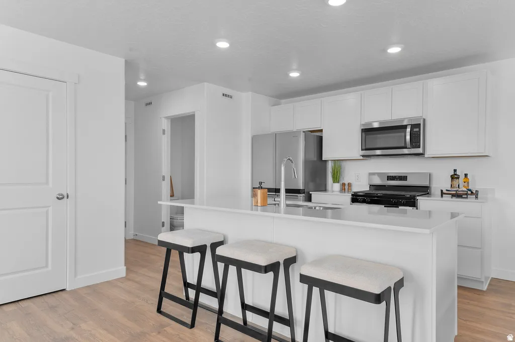 Modern kitchen featuring a large island with seating, stainless steel appliances, white cabinetry, recessed lighting, and wood-finish flooring