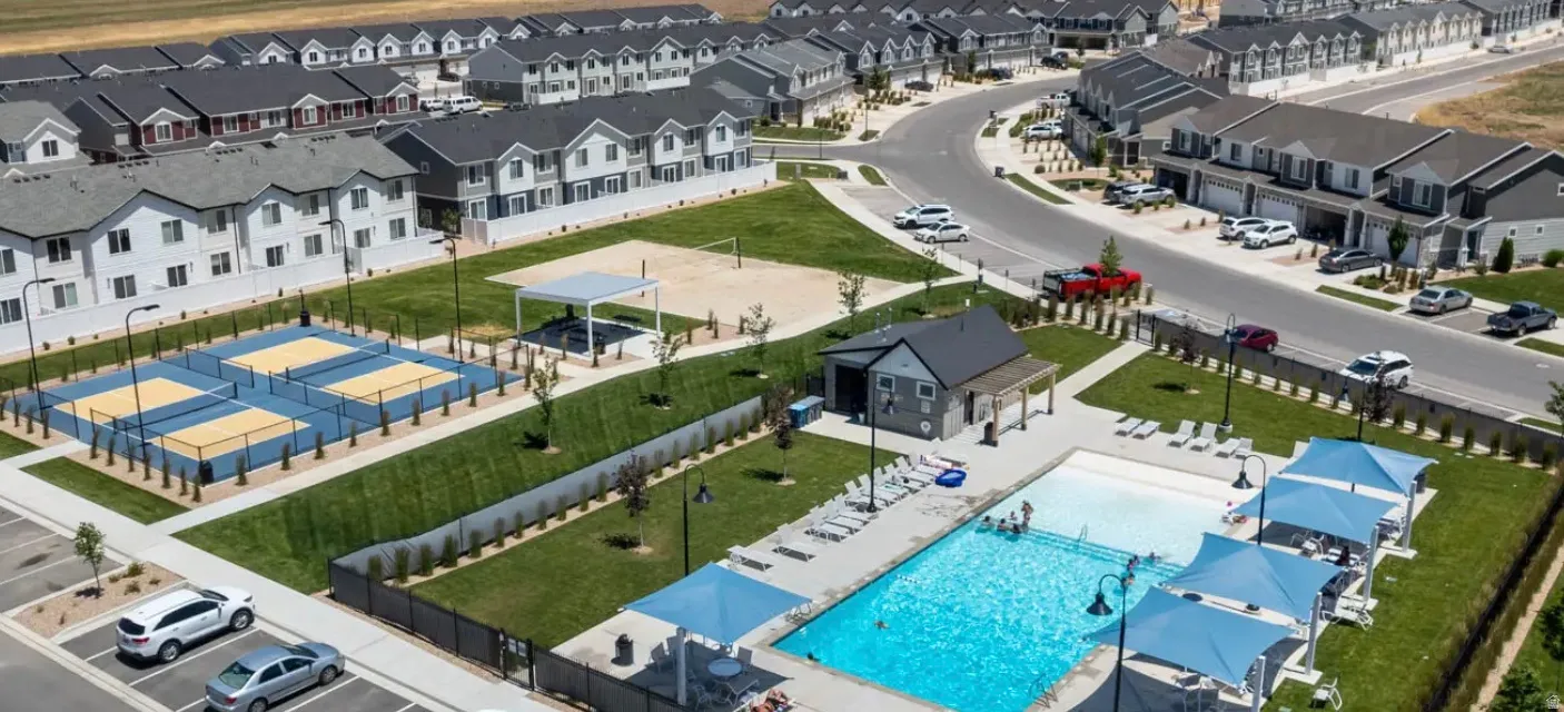 Community recreational amenities featuring multiple pickleball courts, a sand volleyball court, a swimming pool with a shallow entry area, a pool house with a covered patio, and shaded lounge areas