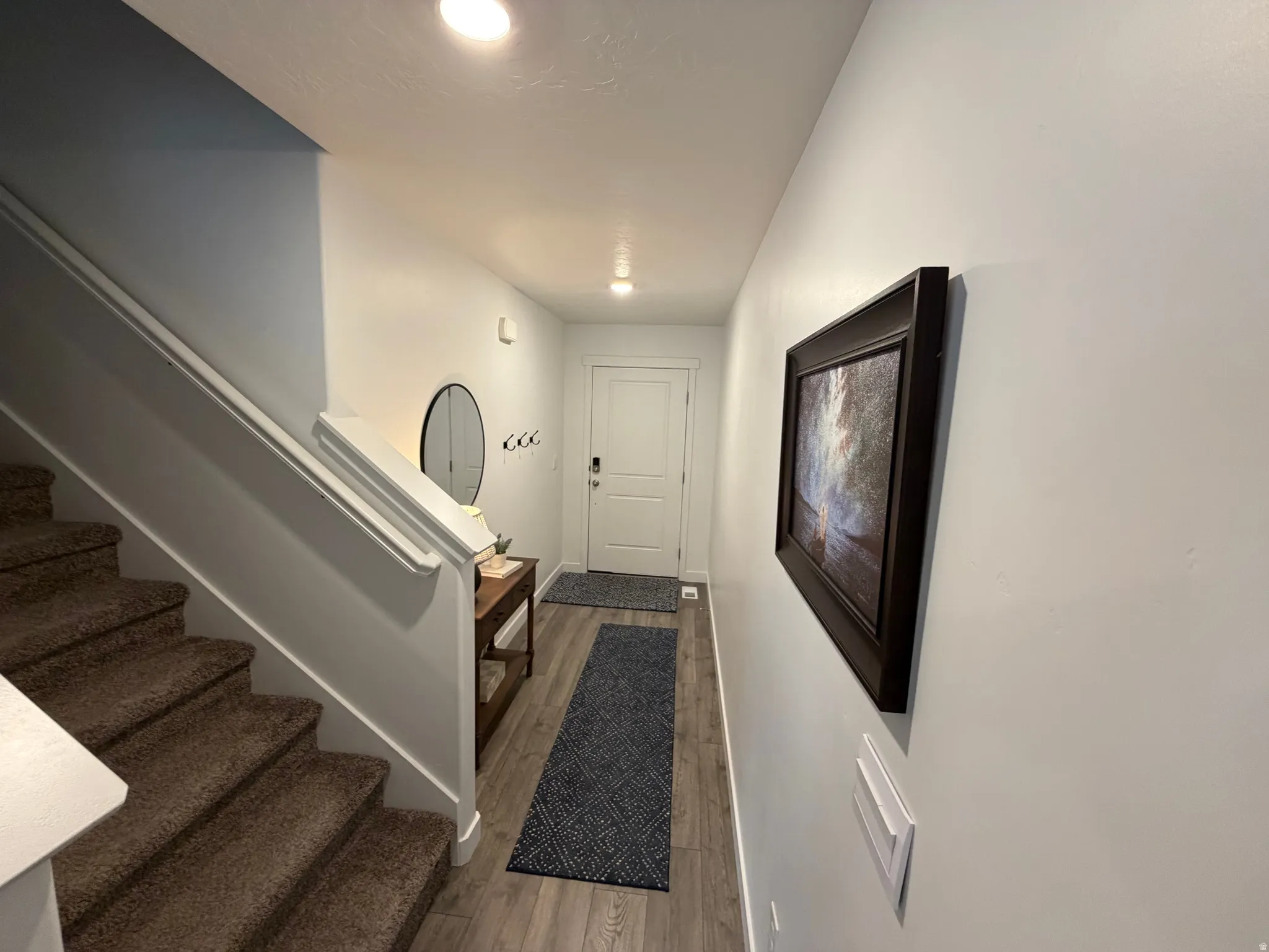 Entryway featuring wood-finish flooring, recessed lighting, white trim, and a carpeted staircase with a white handrail