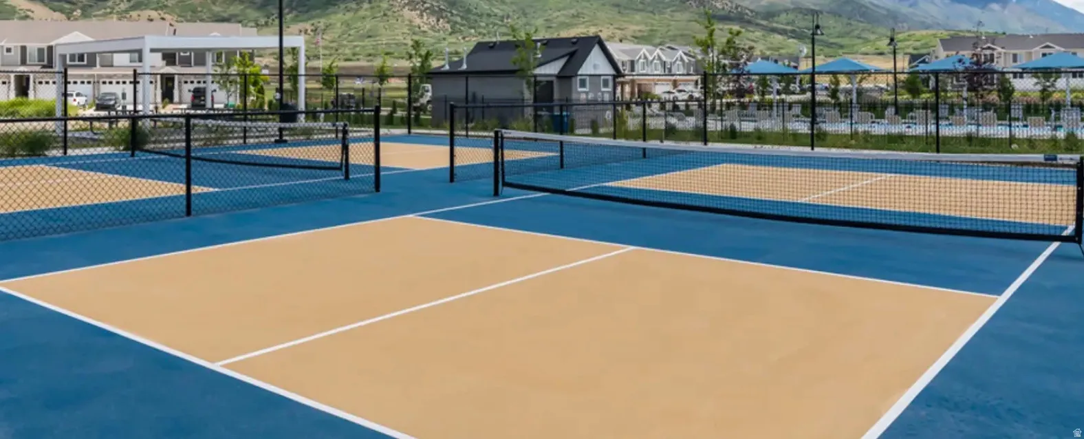 Multiple outdoor pickleball courts featuring blue and tan playing surfaces with white boundary lines and black netting