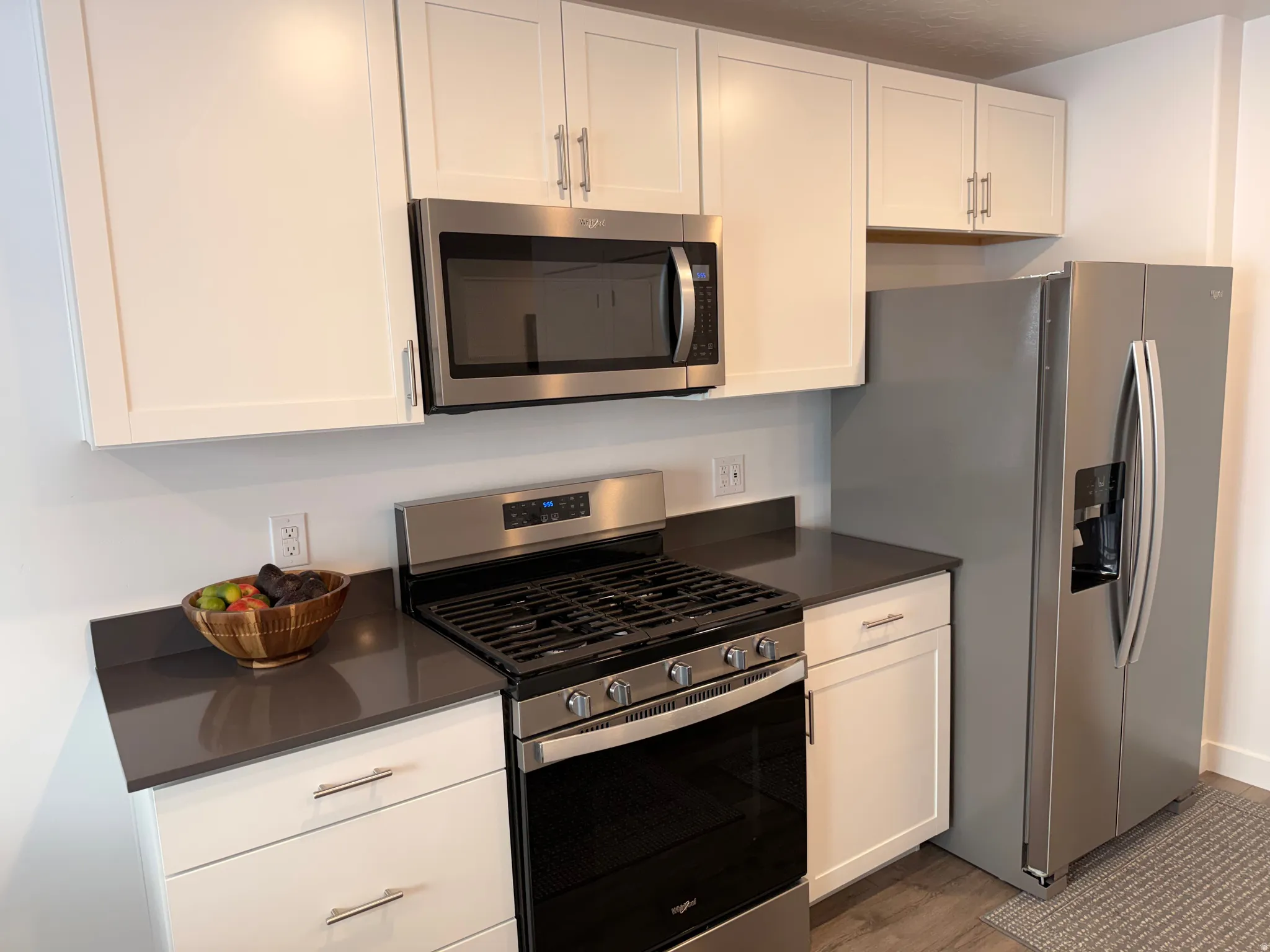 Kitchen featuring white shaker-style cabinetry, dark countertops, and stainless steel appliances including a gas range, microwave, and side-by-side refrigerator