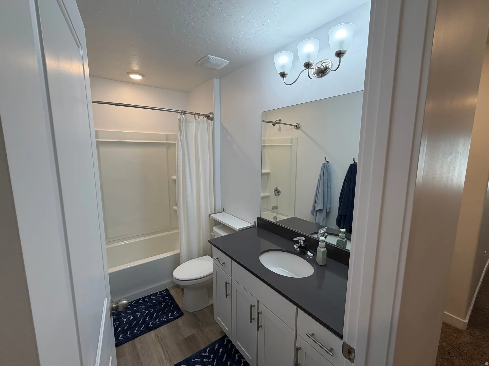Full bathroom featuring a white tub and shower combination, a vanity with a dark countertop and undermount sink, white cabinetry with silver hardware, and wood-finish flooring