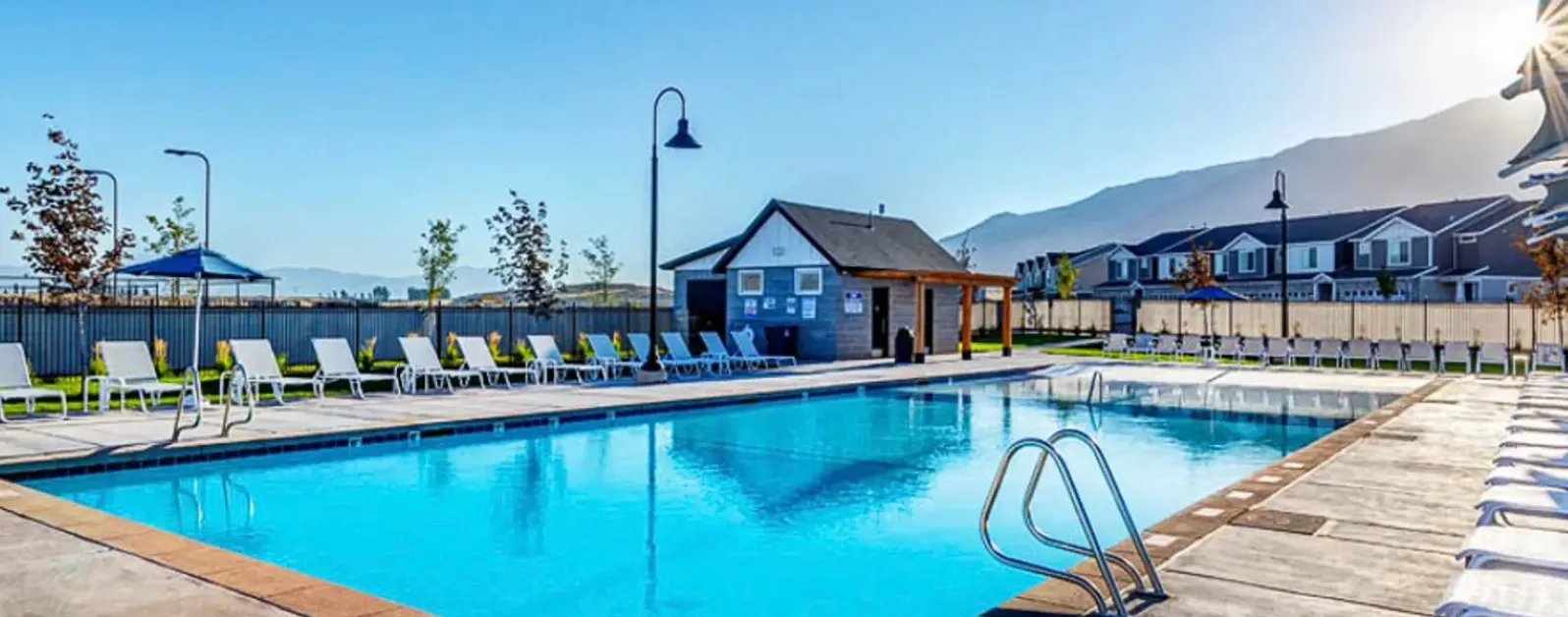 Community swimming pool with a concrete deck, pool house, and sun loungers