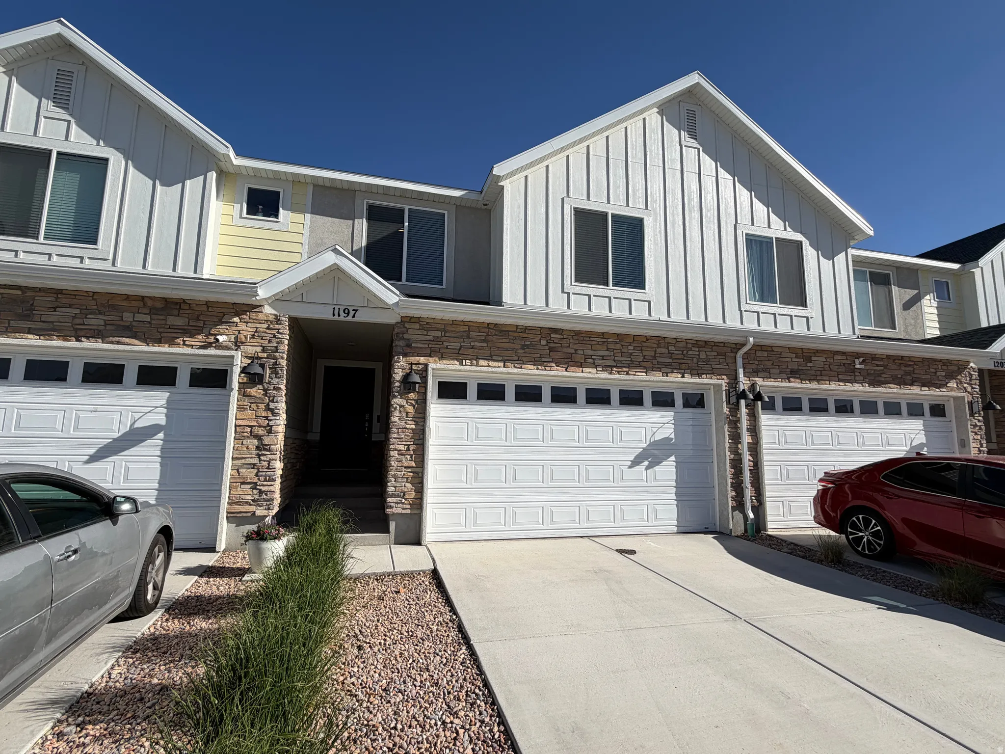 Townhome exterior featuring stacked stone accents, vertical white siding, and an attached two-car garage