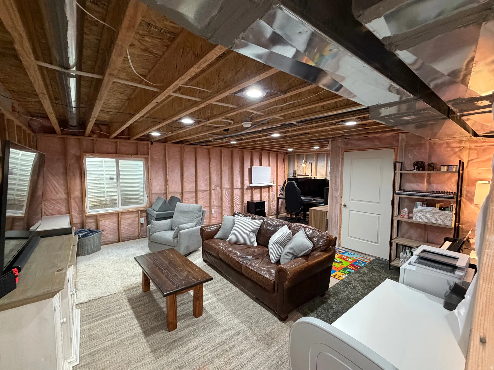 Unfinished basement area featuring exposed ceiling joists and ductwork, recessed lighting, a single window, a white interior door, and partial wall insulation