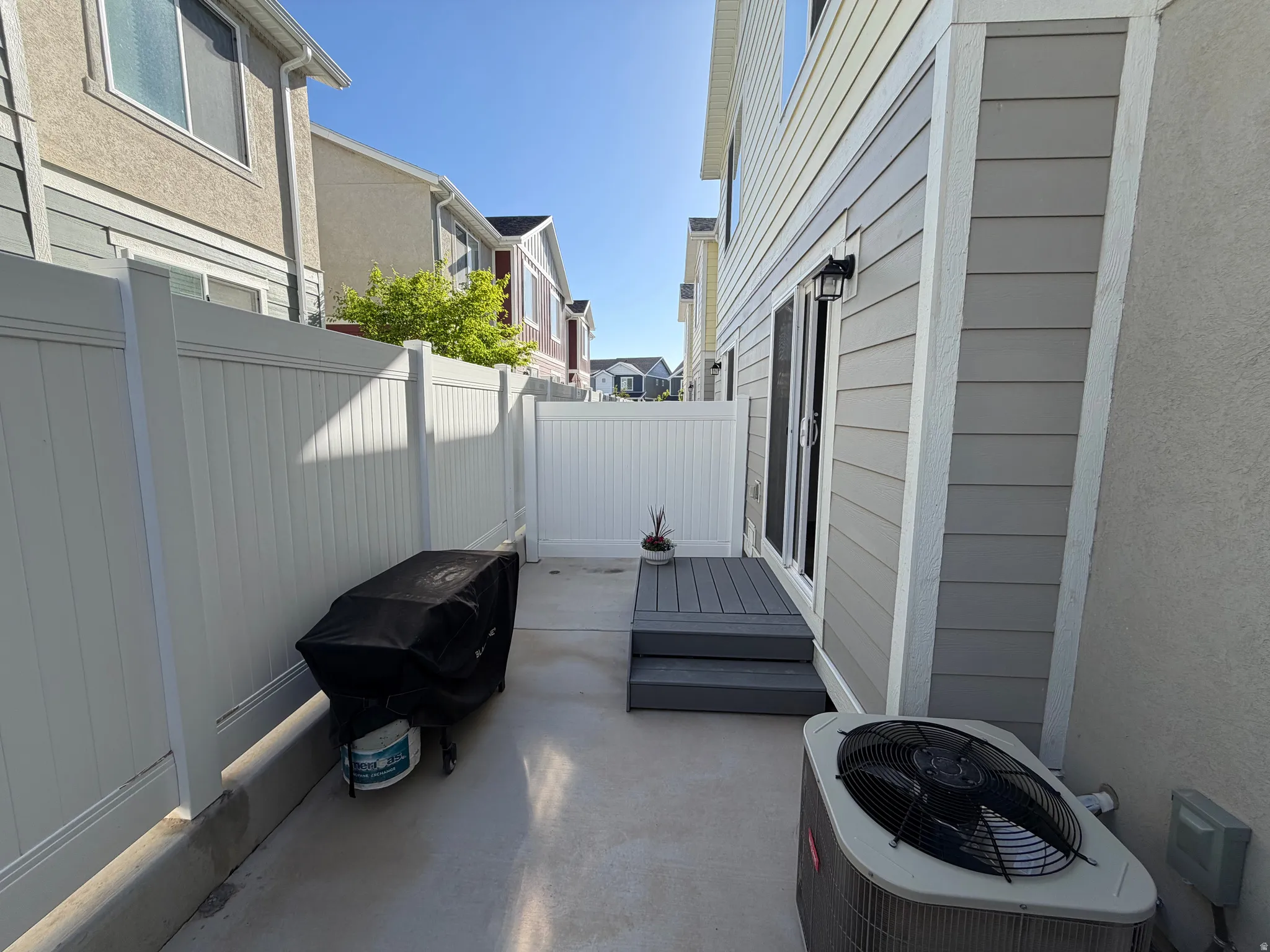 Private patio area featuring a white vinyl fence, sliding glass door access, and a multi-level deck