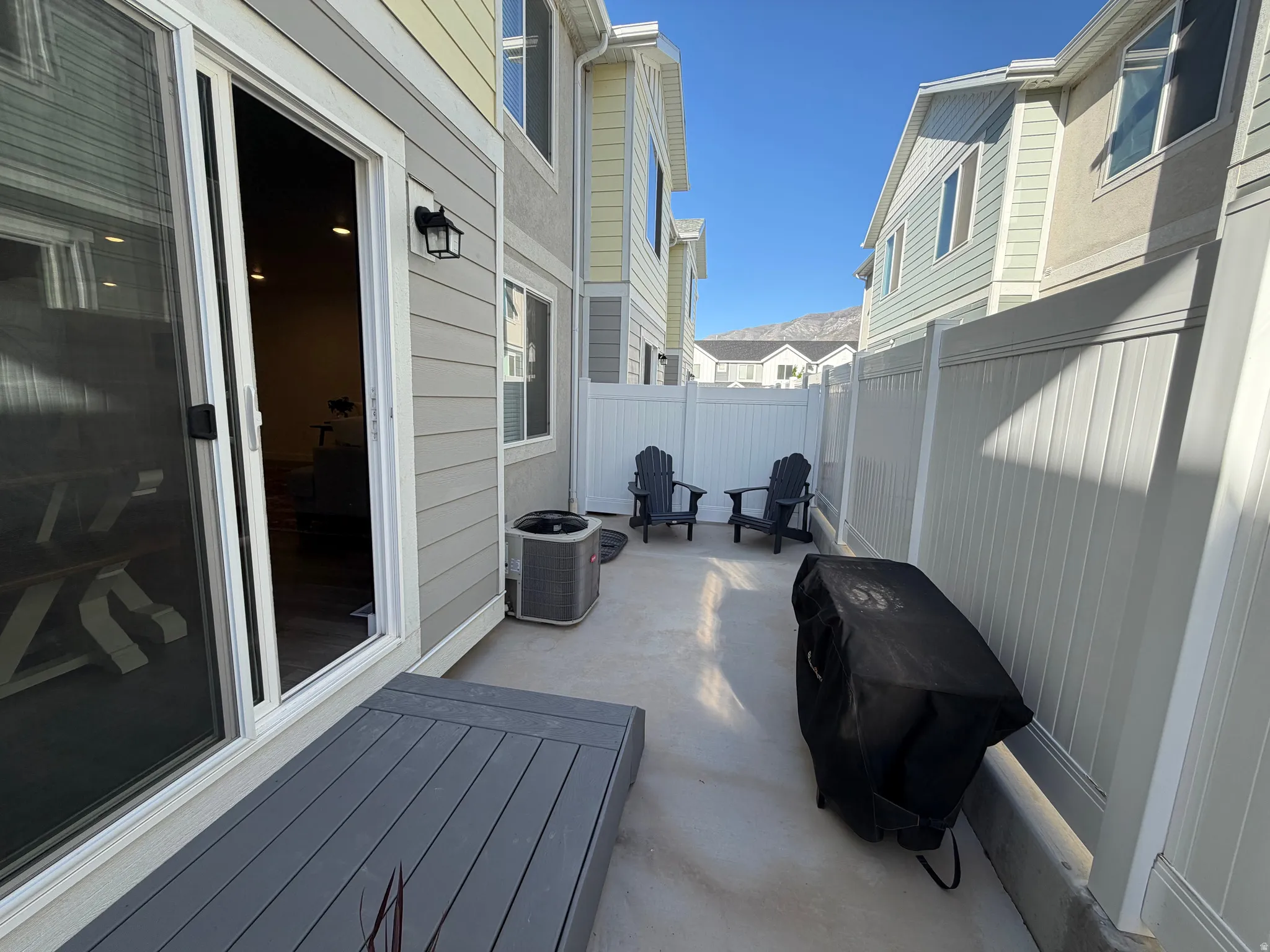 Private concrete patio area featuring white privacy fencing, a gray composite deck, and direct access through a sliding glass door