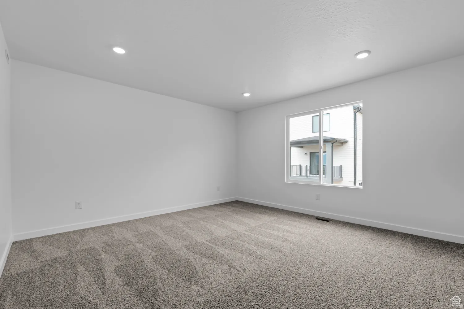 Spacious room featuring neutral carpeting, crisp white walls, recessed lighting, and a prominent window