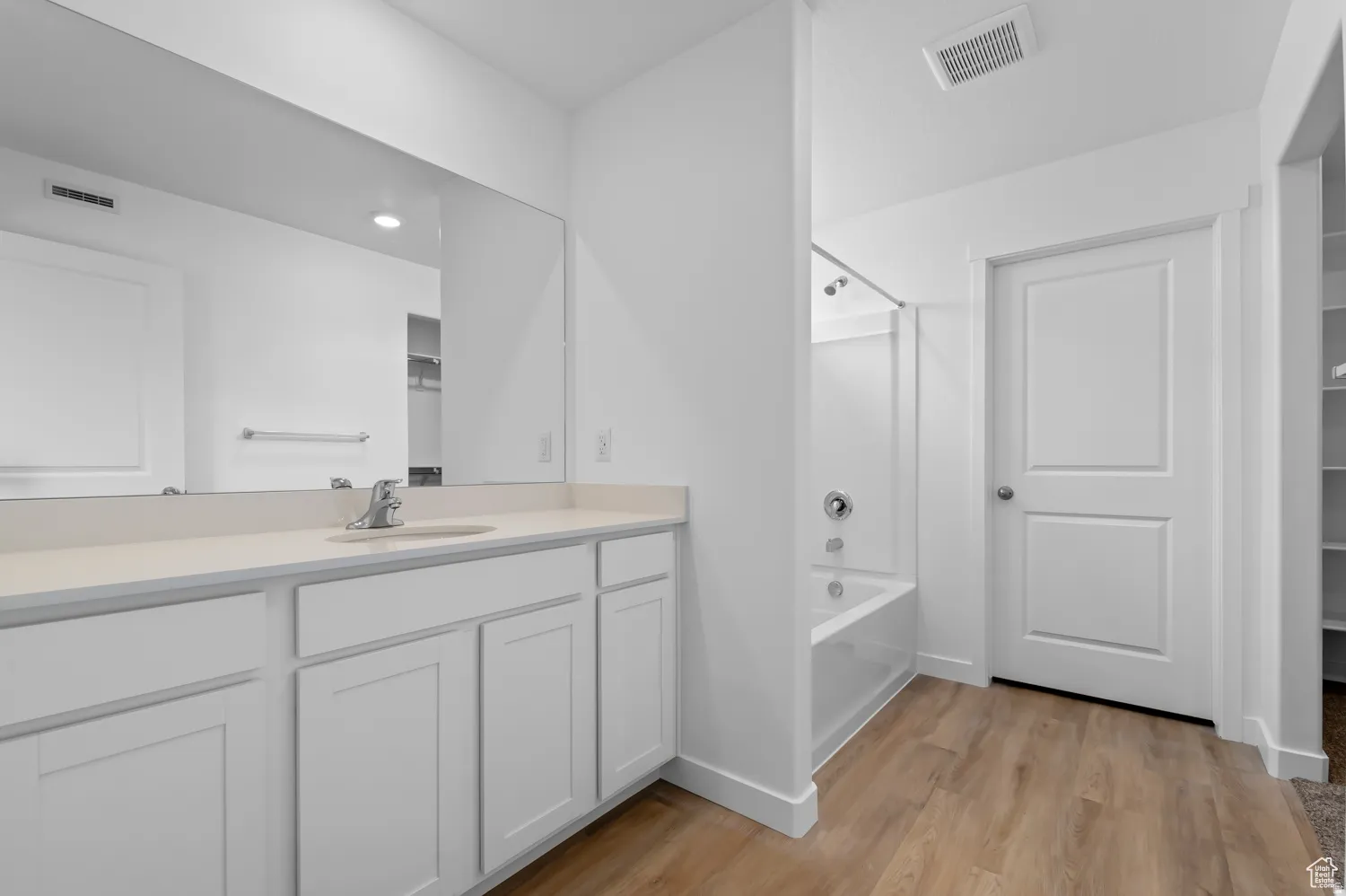 Bathroom featuring a light wood-finish floor, a white vanity with an undermount sink, a large wall-mounted mirror, a tub/shower combination, and white interior doors